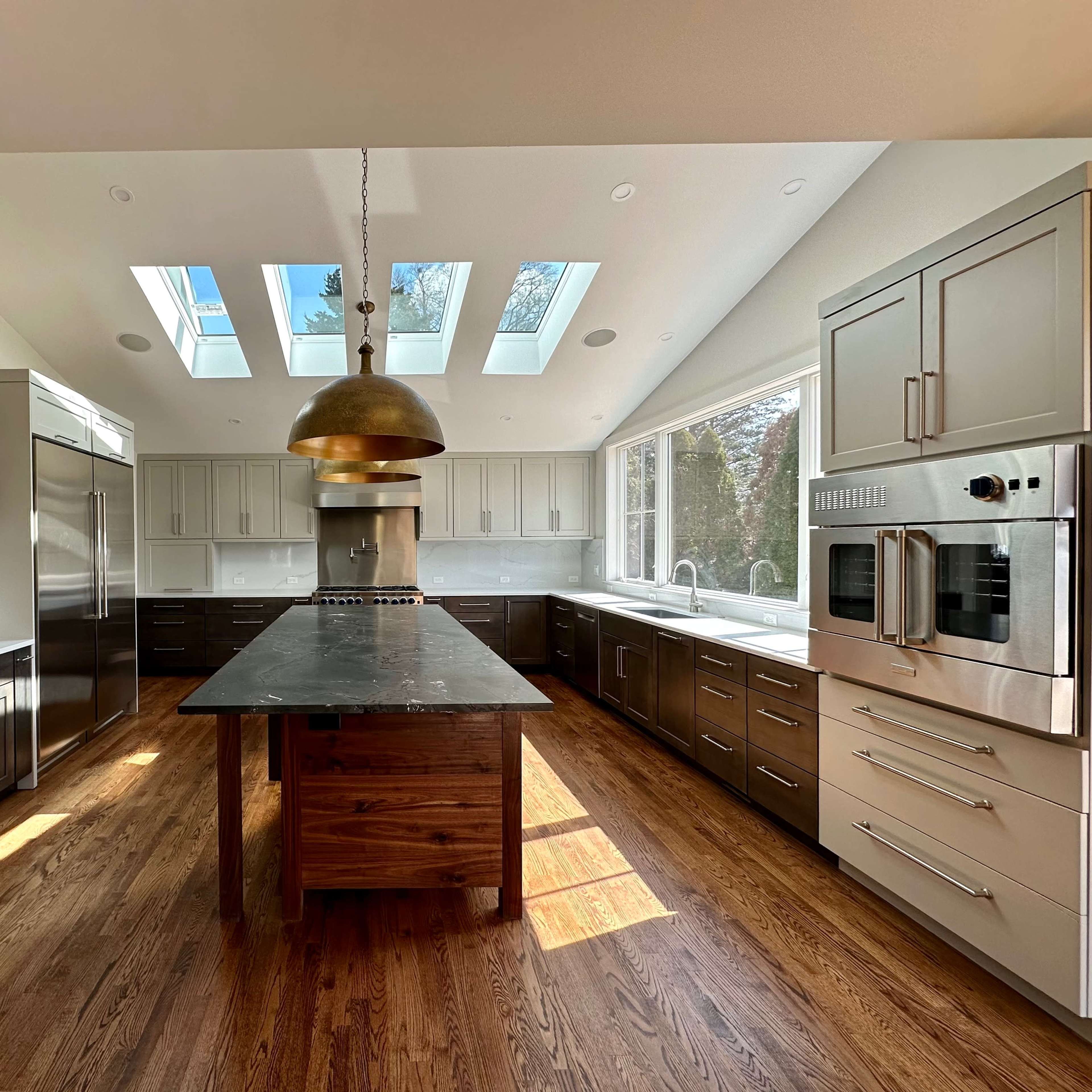 A modern kitchen features a central island with a dark countertop, stainless steel appliances, and large skylights illuminating the space.