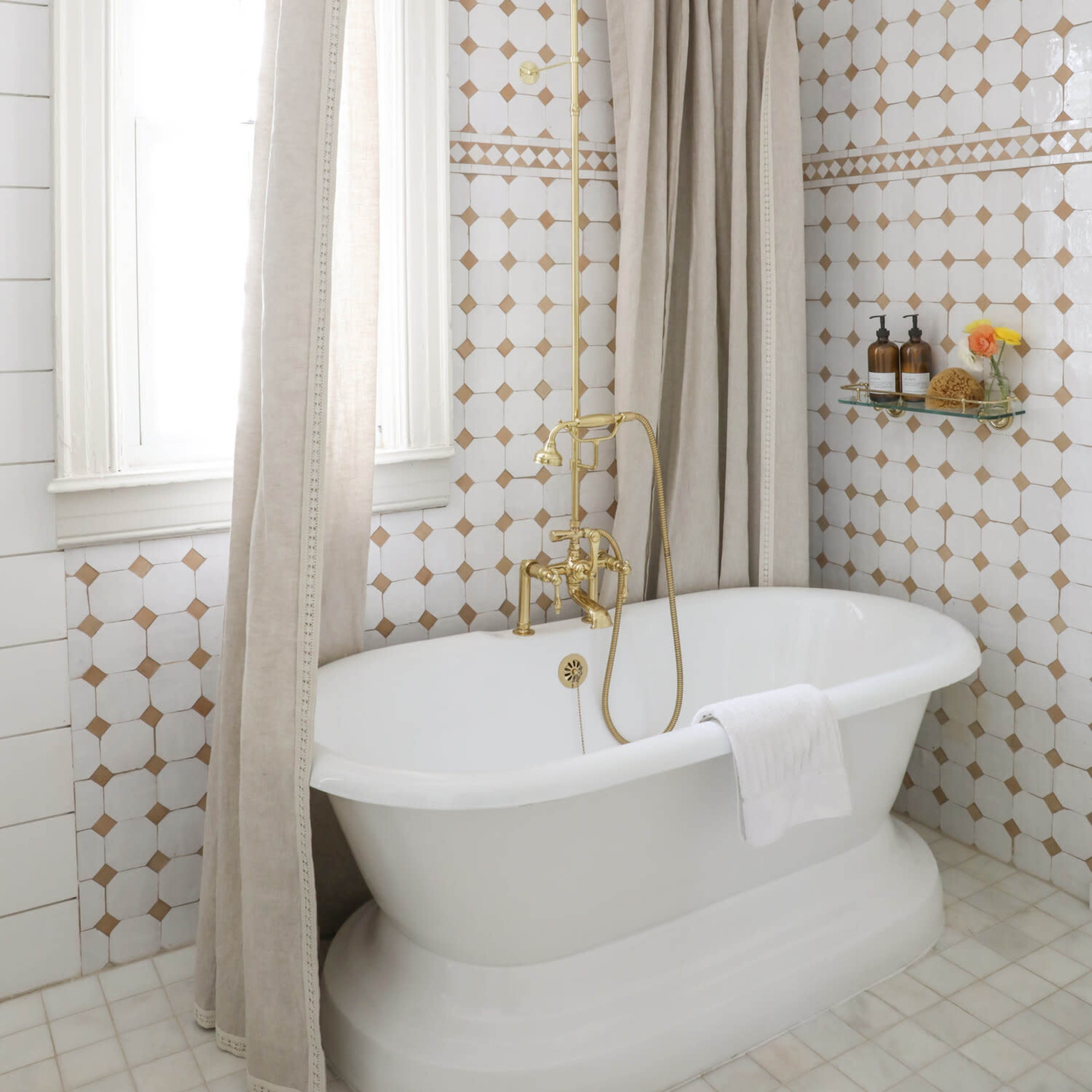 A bathroom featuring a freestanding white bathtub, a gold shower fixture, and a tiled wall with a geometric pattern.