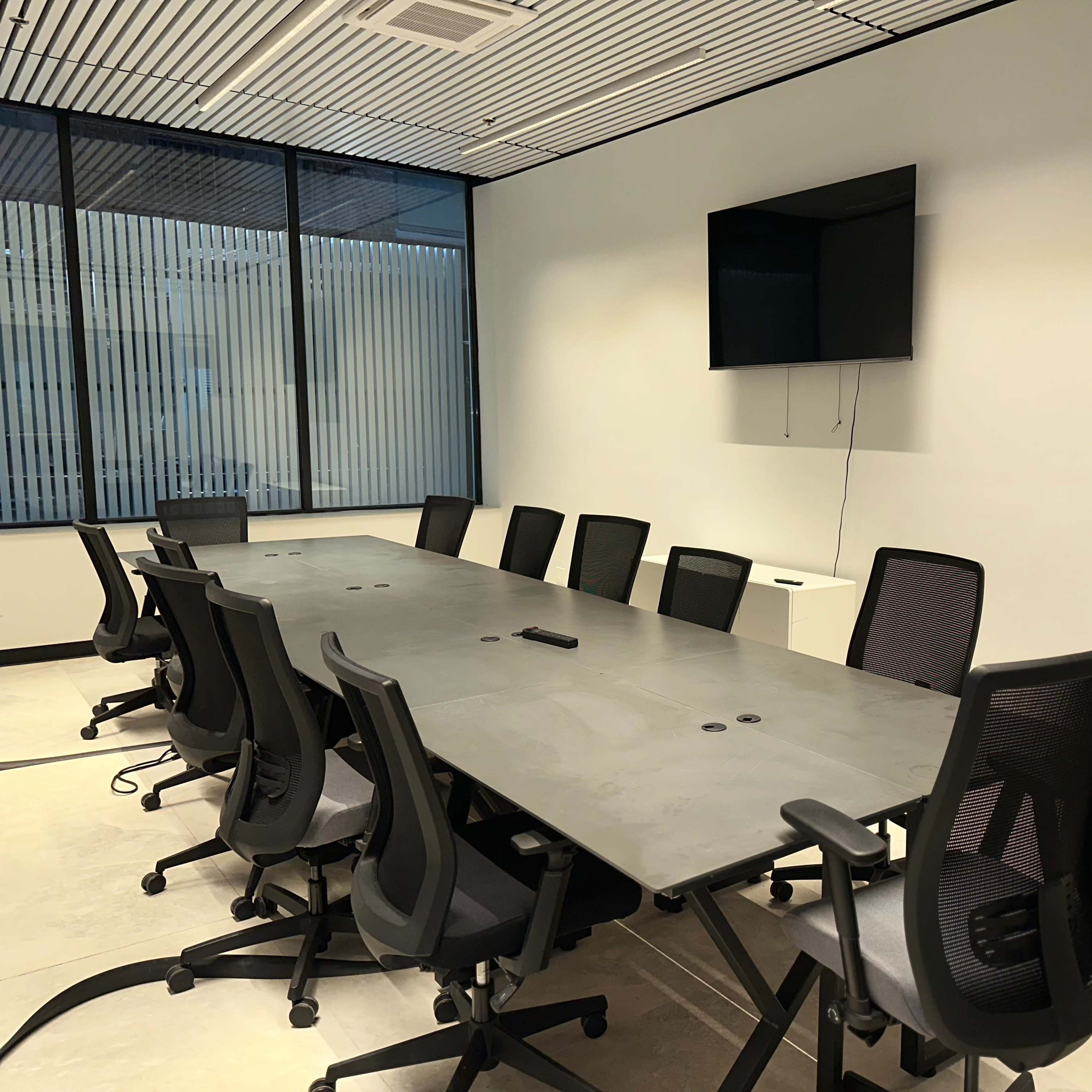 A large conference room features a long, rectangular table surrounded by multiple office chairs, with a television mounted on the wall and a whiteboard on one side.