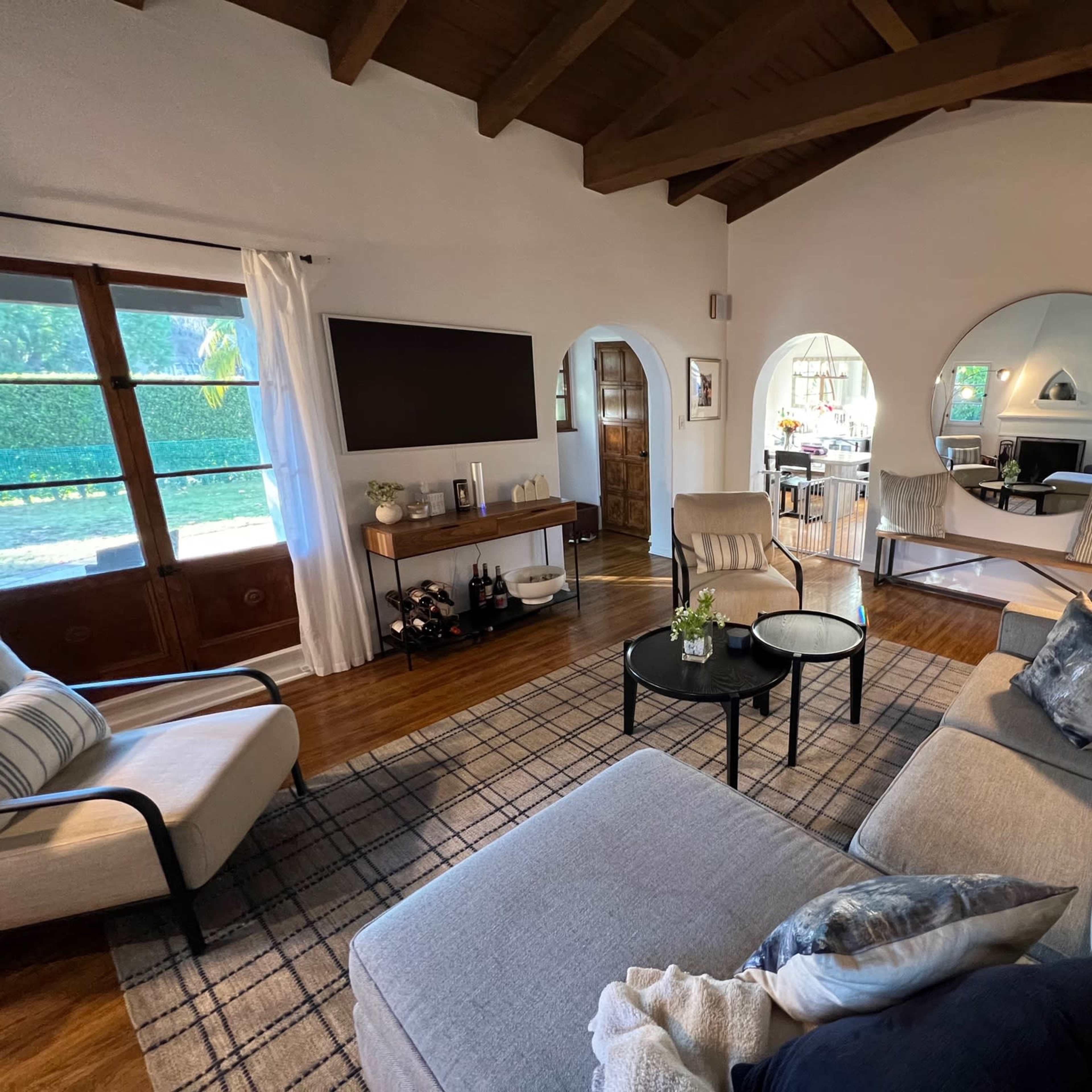 A cozy living room with large windows, a sectional sofa, a coffee table, and round mirrors on the wall.