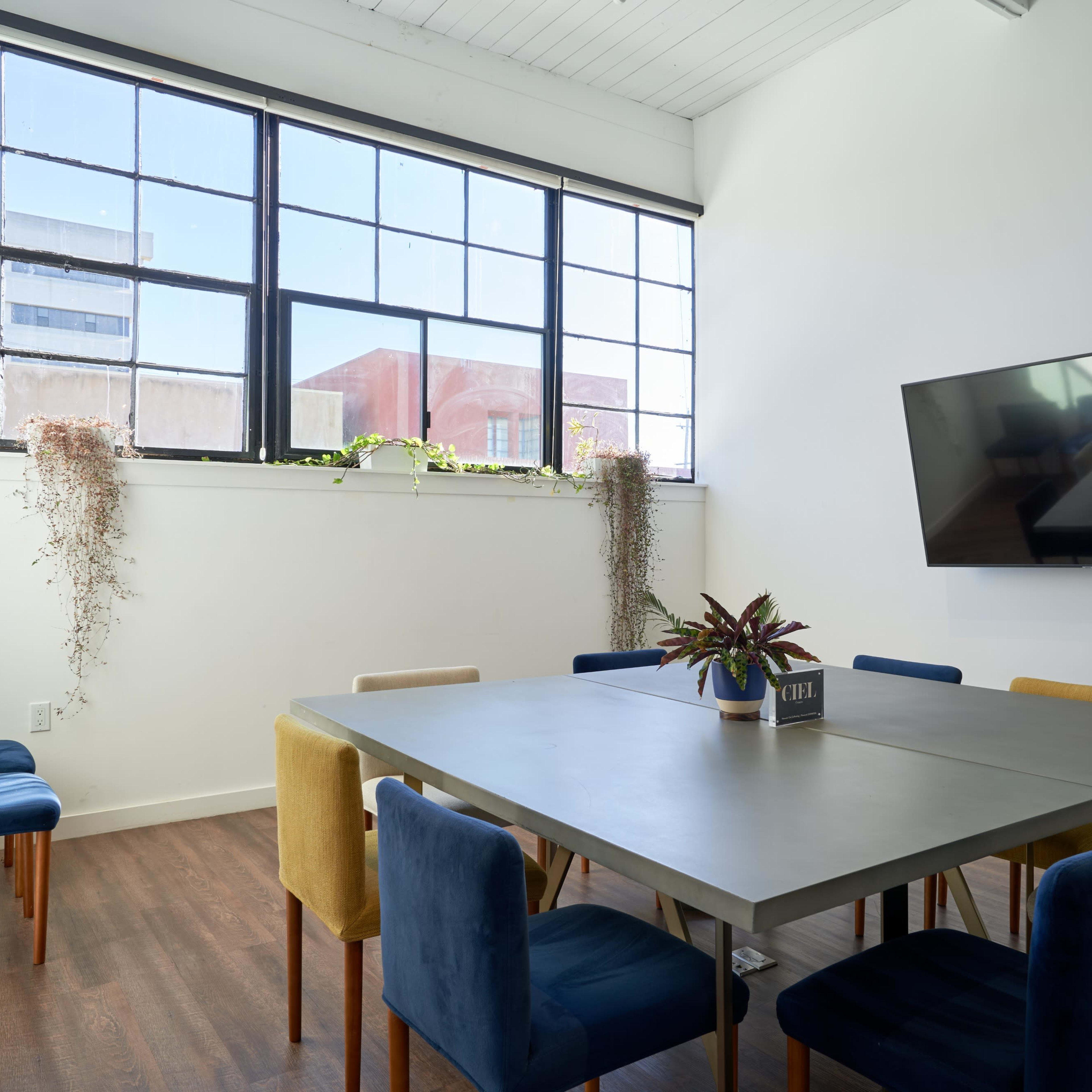 A bright meeting room with a large table surrounded by colorful chairs and a wall-mounted television.