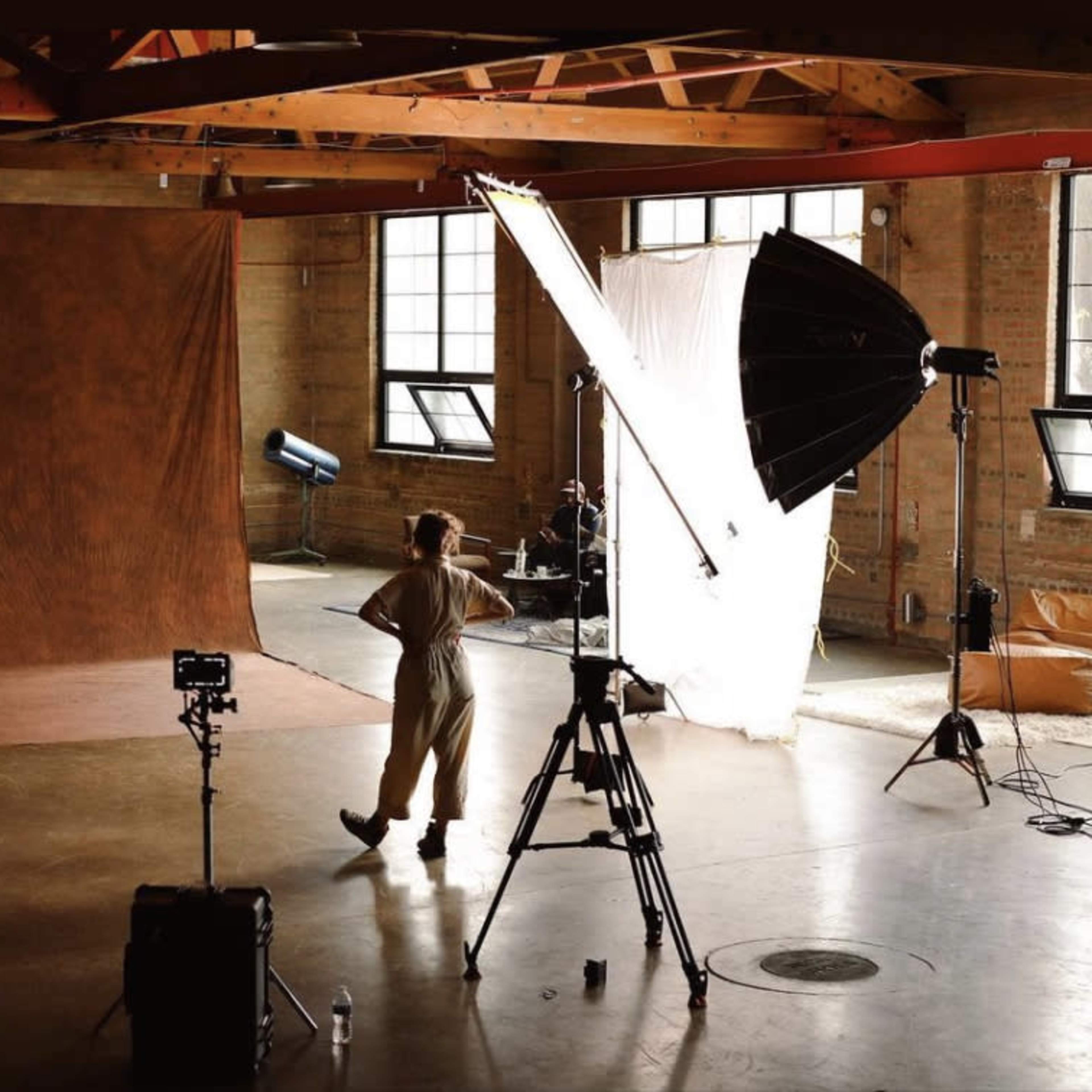A photography studio features multiple backdrops, lighting equipment, and a person in front of a brown backdrop.