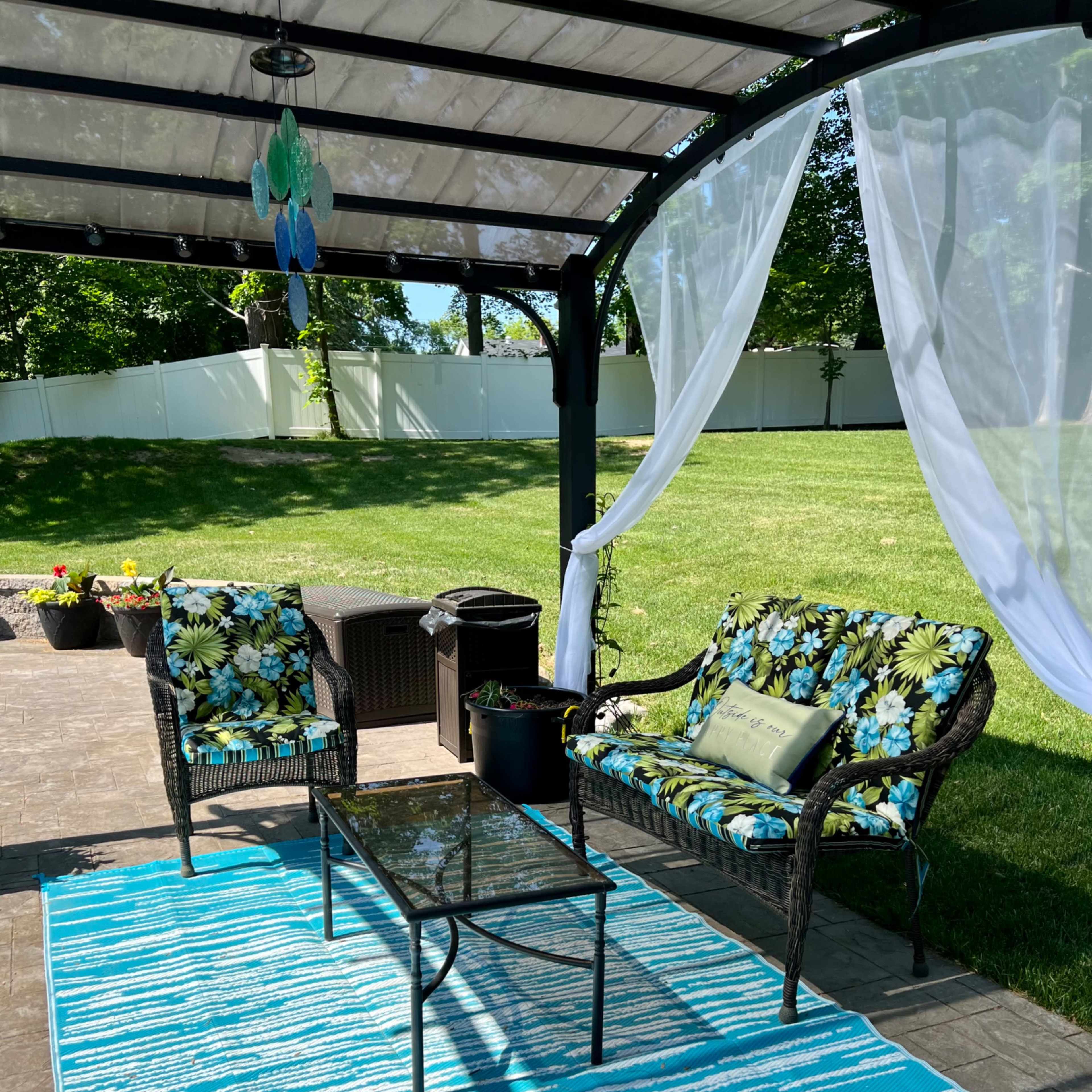 A covered outdoor seating area features two floral-patterned chairs and a glass table on a blue striped rug.