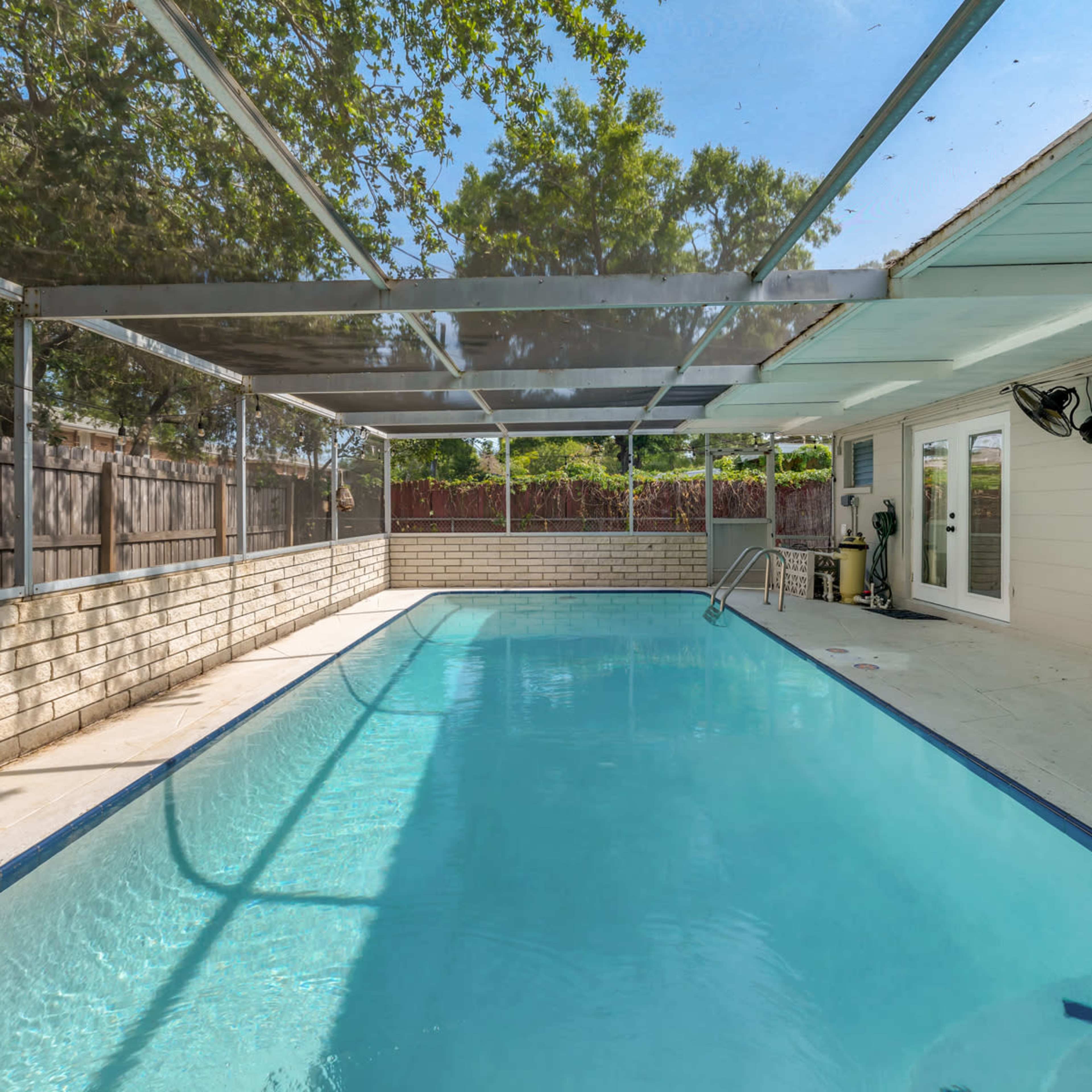 A screened-in swimming pool surrounded by a patio area and a neighboring fence.