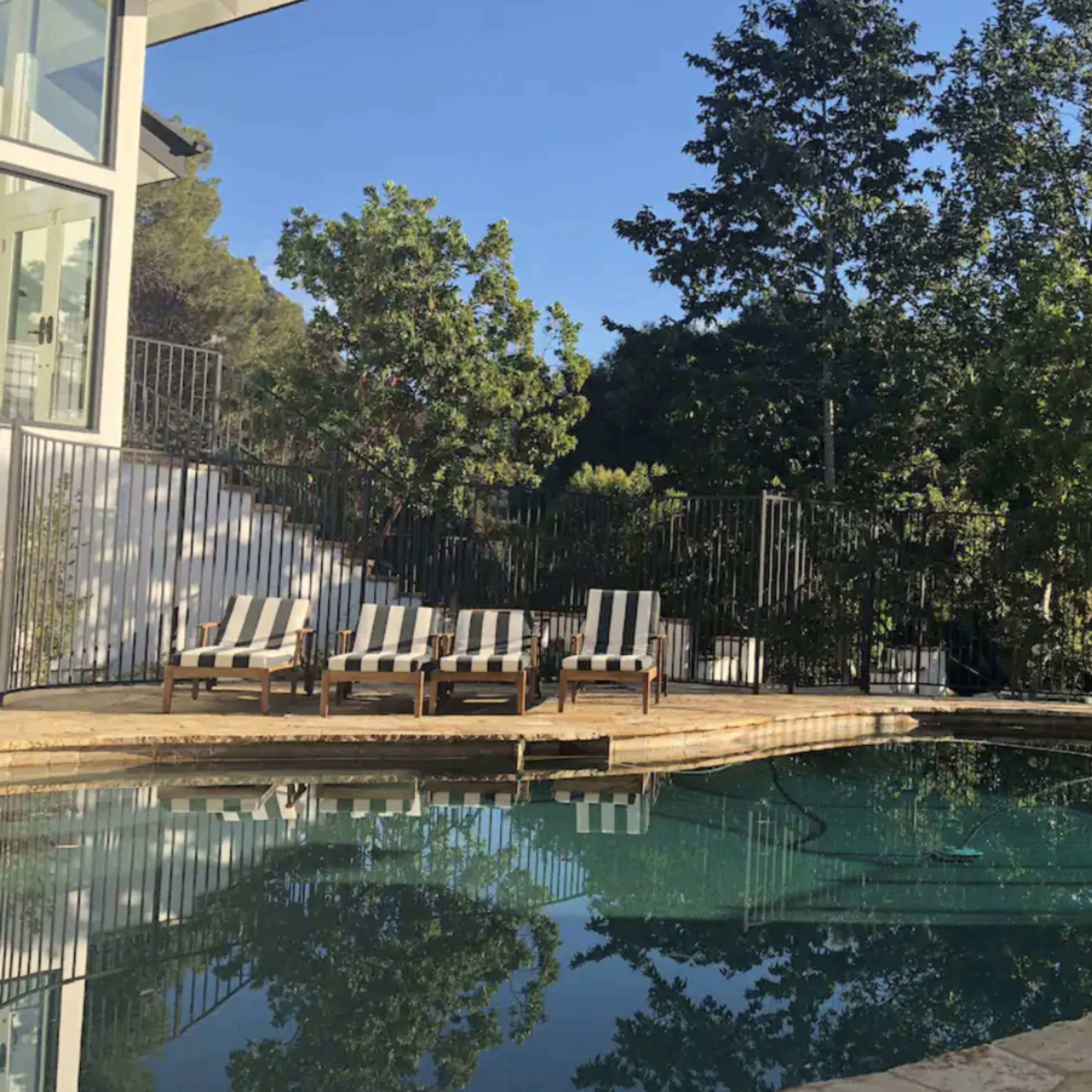 A circular swimming pool is surrounded by lounge chairs and lush green trees.