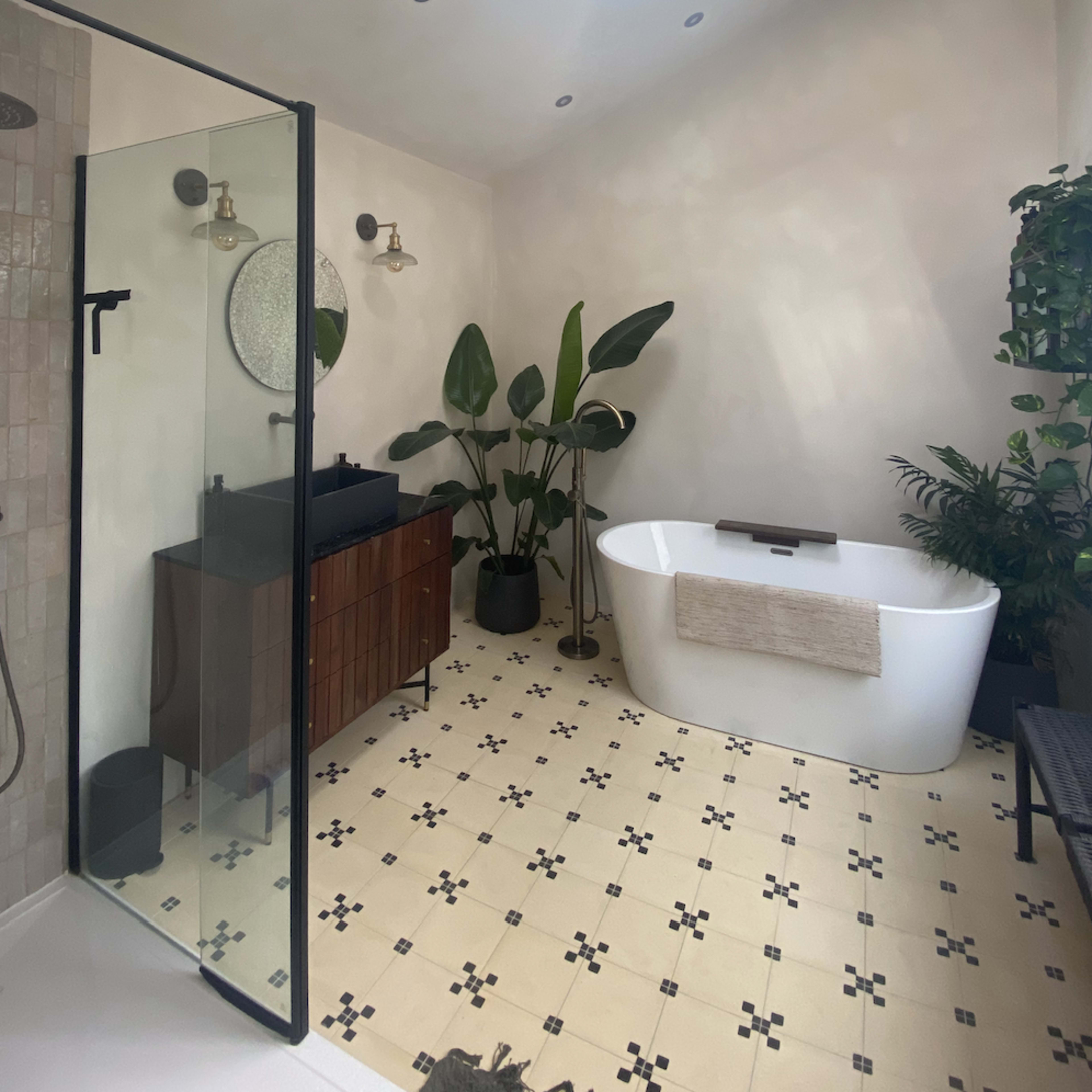 A modern bathroom features a freestanding tub, a glass shower, a wooden vanity, and several potted plants under a skylight.