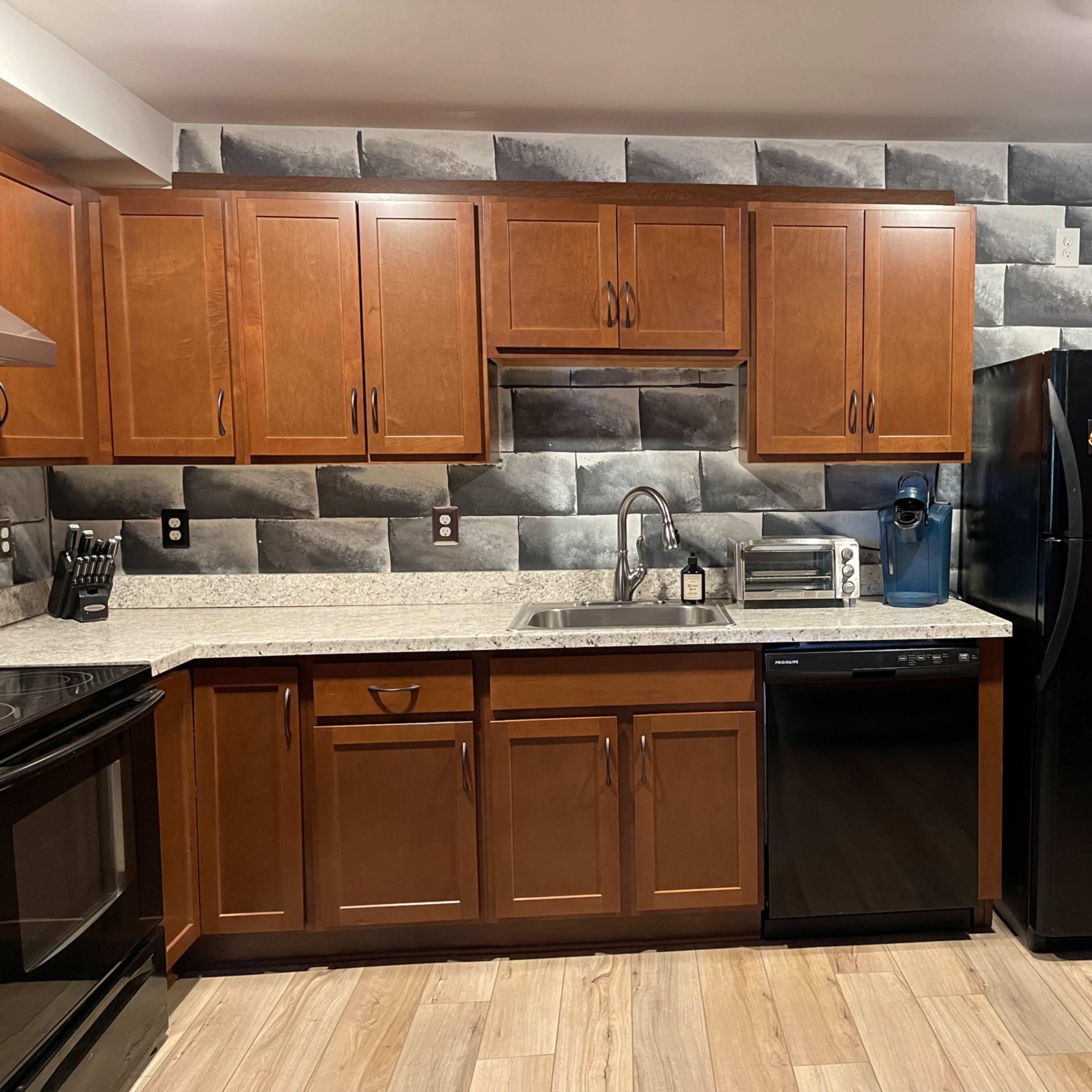 A modern kitchen with dark wooden cabinets, a stainless steel sink, and a black refrigerator, all set against a textured gray wall.