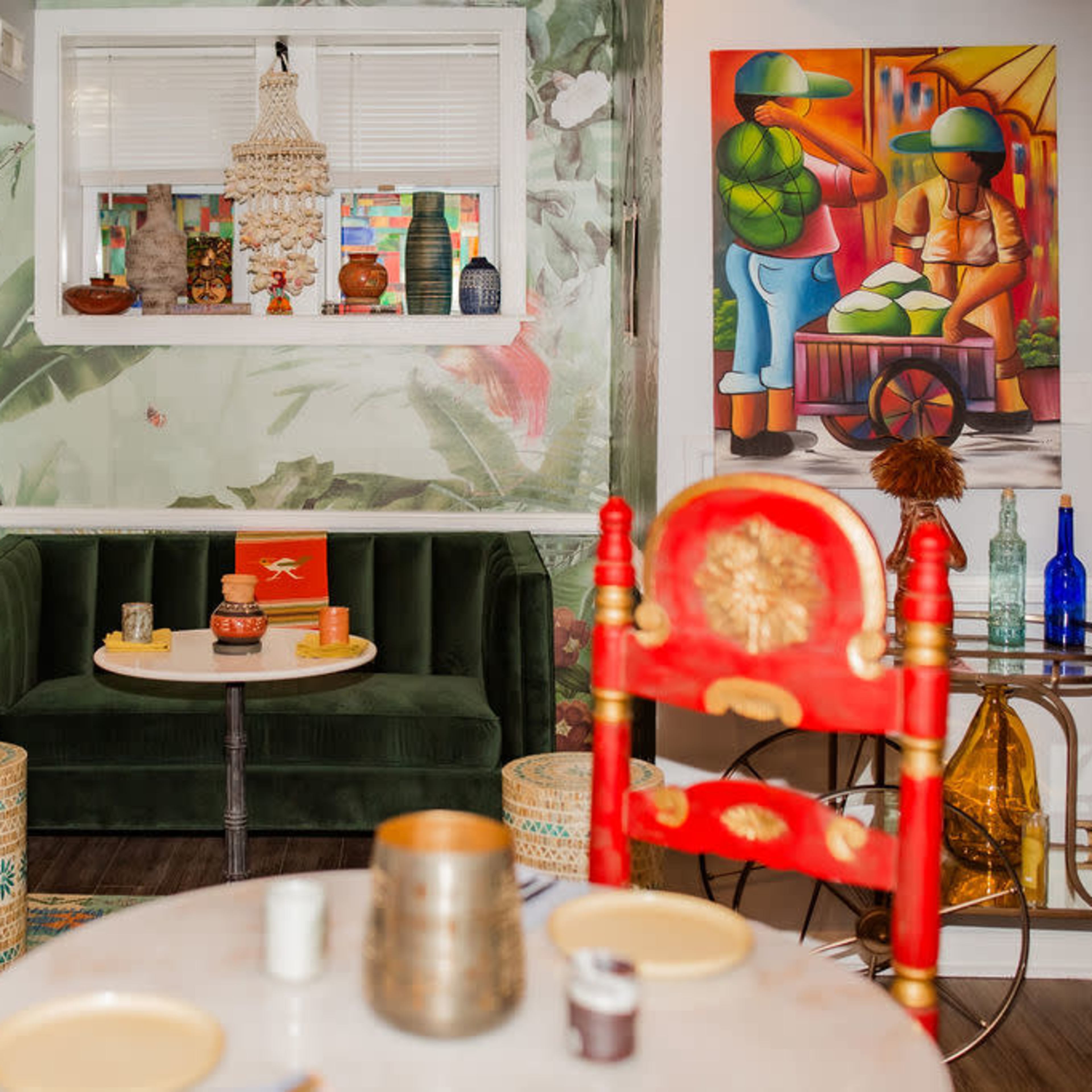 A colorful interior of a dining area featuring a green sofa, a round table with decorative items, and vibrant wall art with a tropical theme.