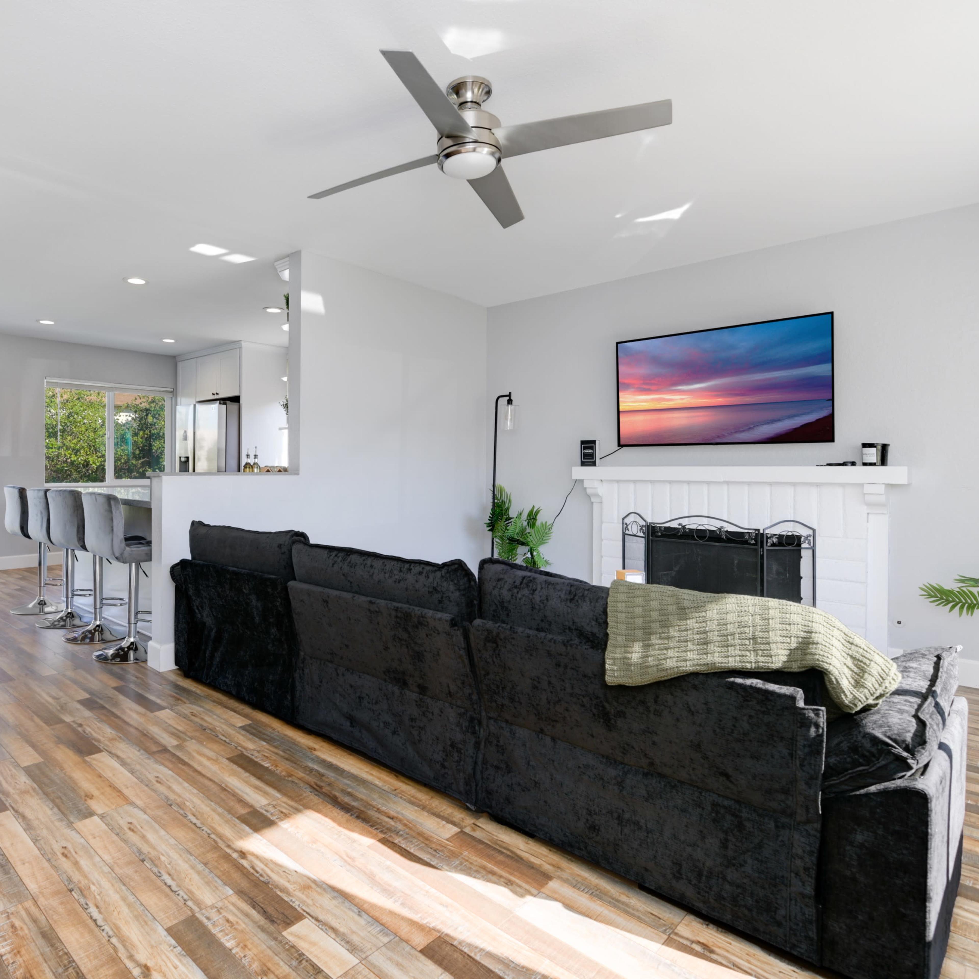A modern living room features a black sofa, a wall-mounted television, and a sliding glass door opening to an outdoor space.