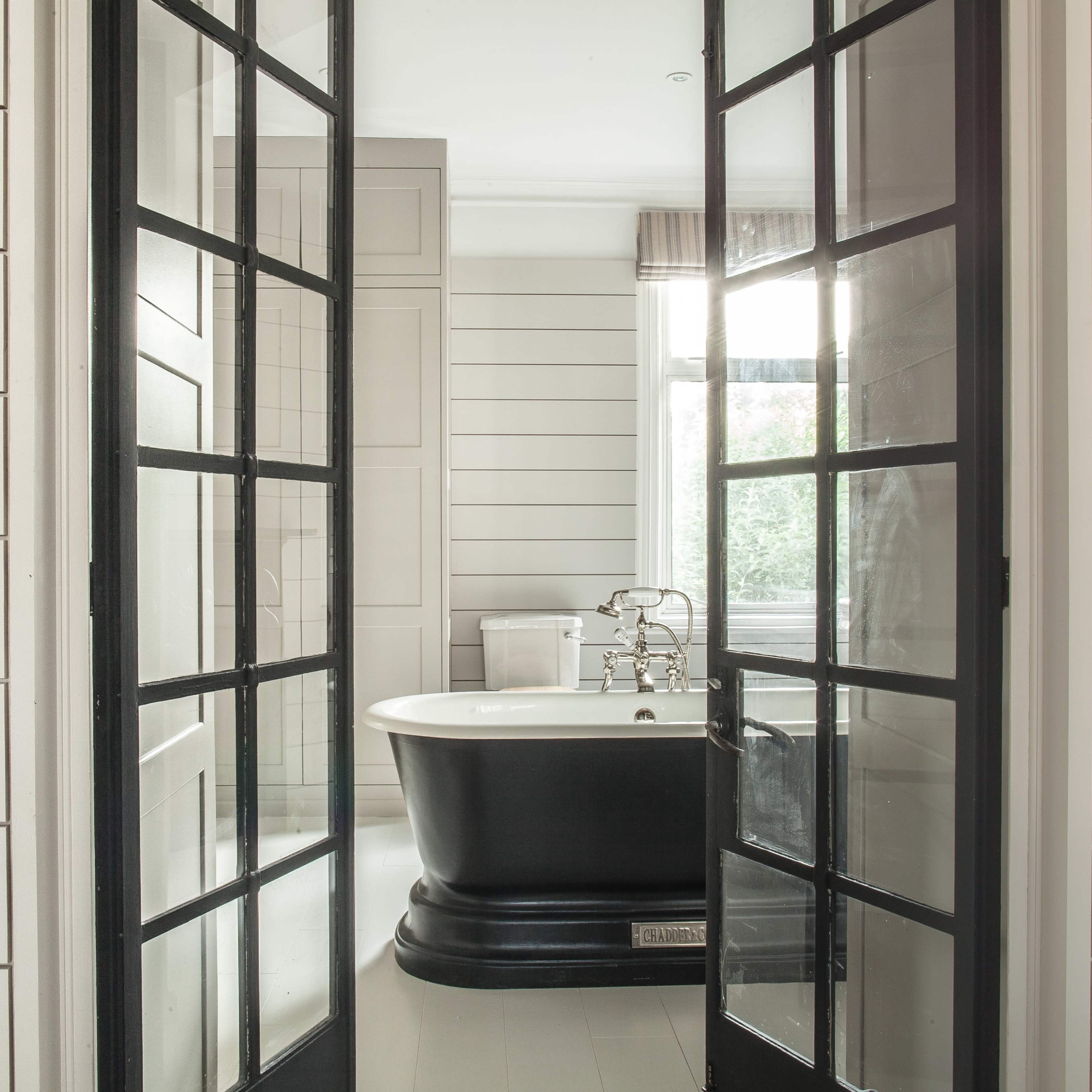 A modern bathroom with a black freestanding bathtub framed by large black glass doors.