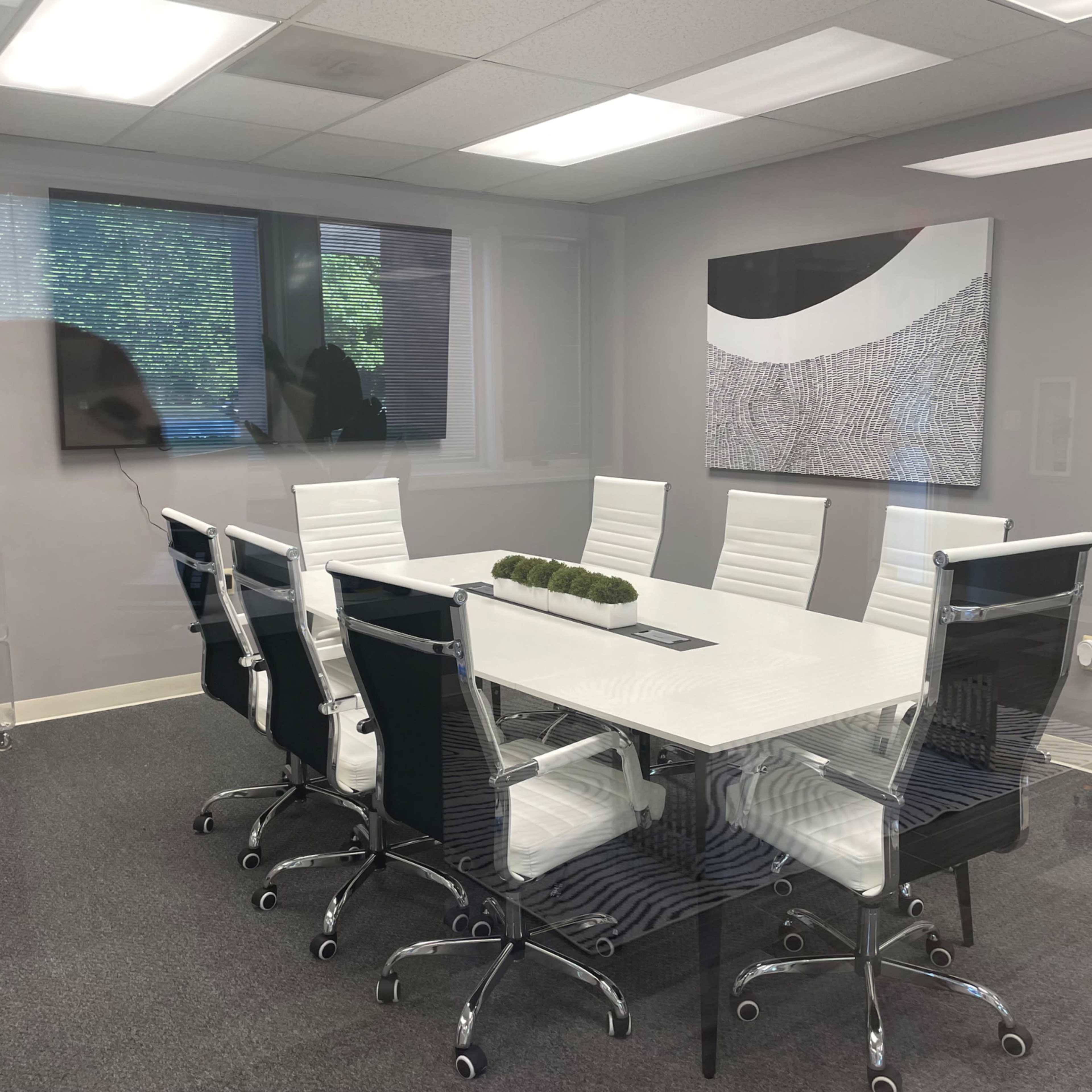 A modern conference room with a rectangular white table surrounded by black and white chairs, and two large screens mounted on the walls.