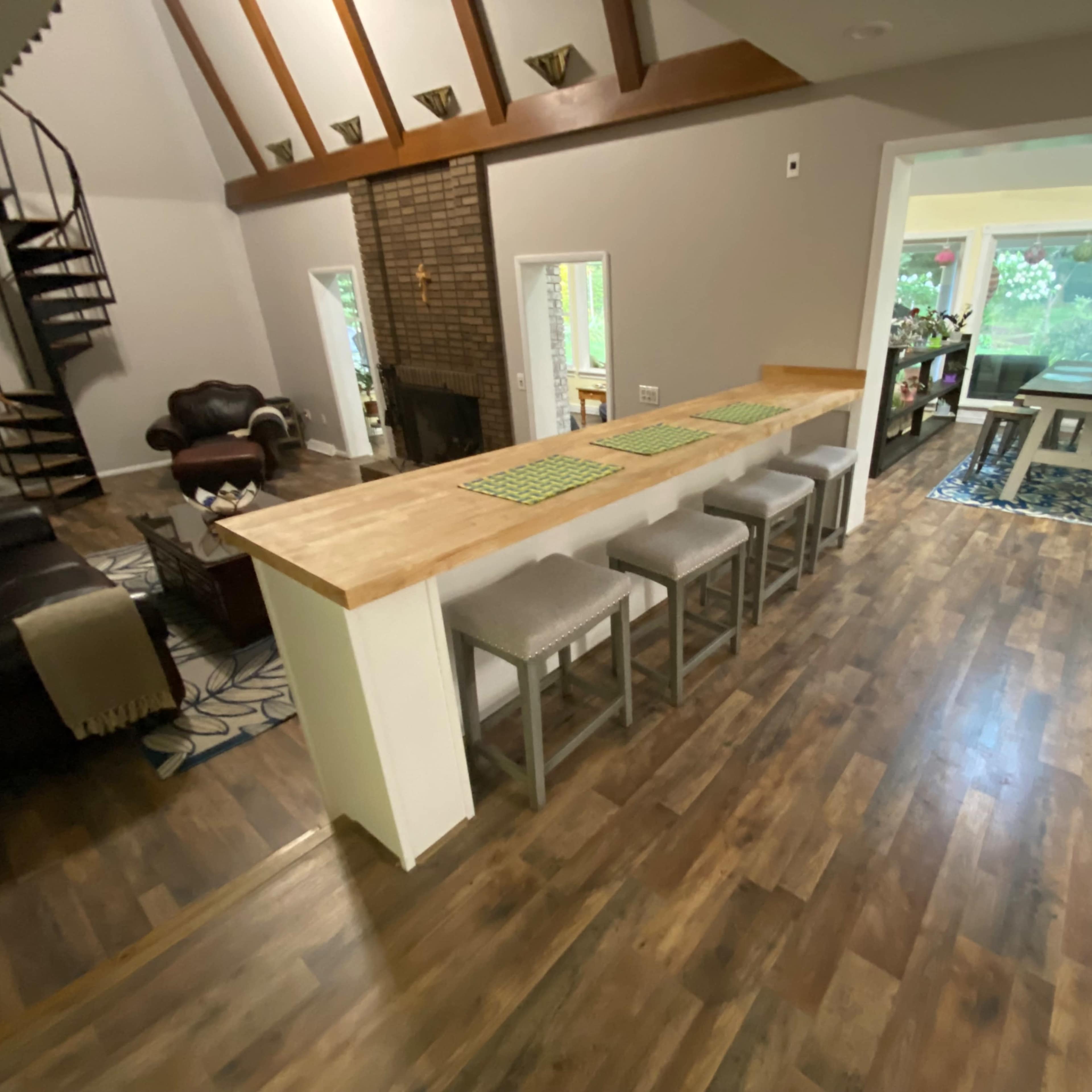 A spacious living area with a large wooden counter, seating for eight, and a view of a dining area through large windows.