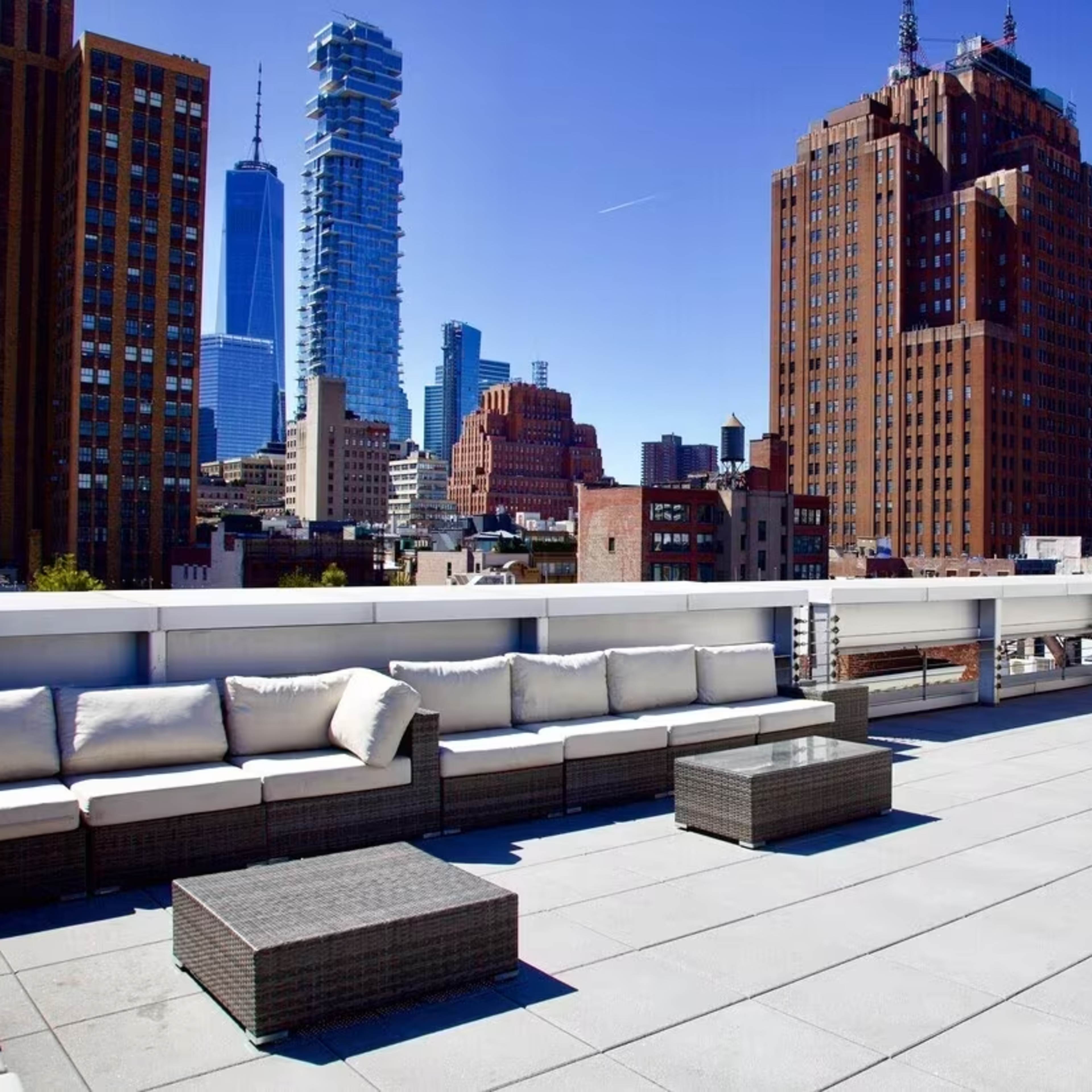 A rooftop terrace features modern seating and tables, overlooking a city skyline with tall buildings.
