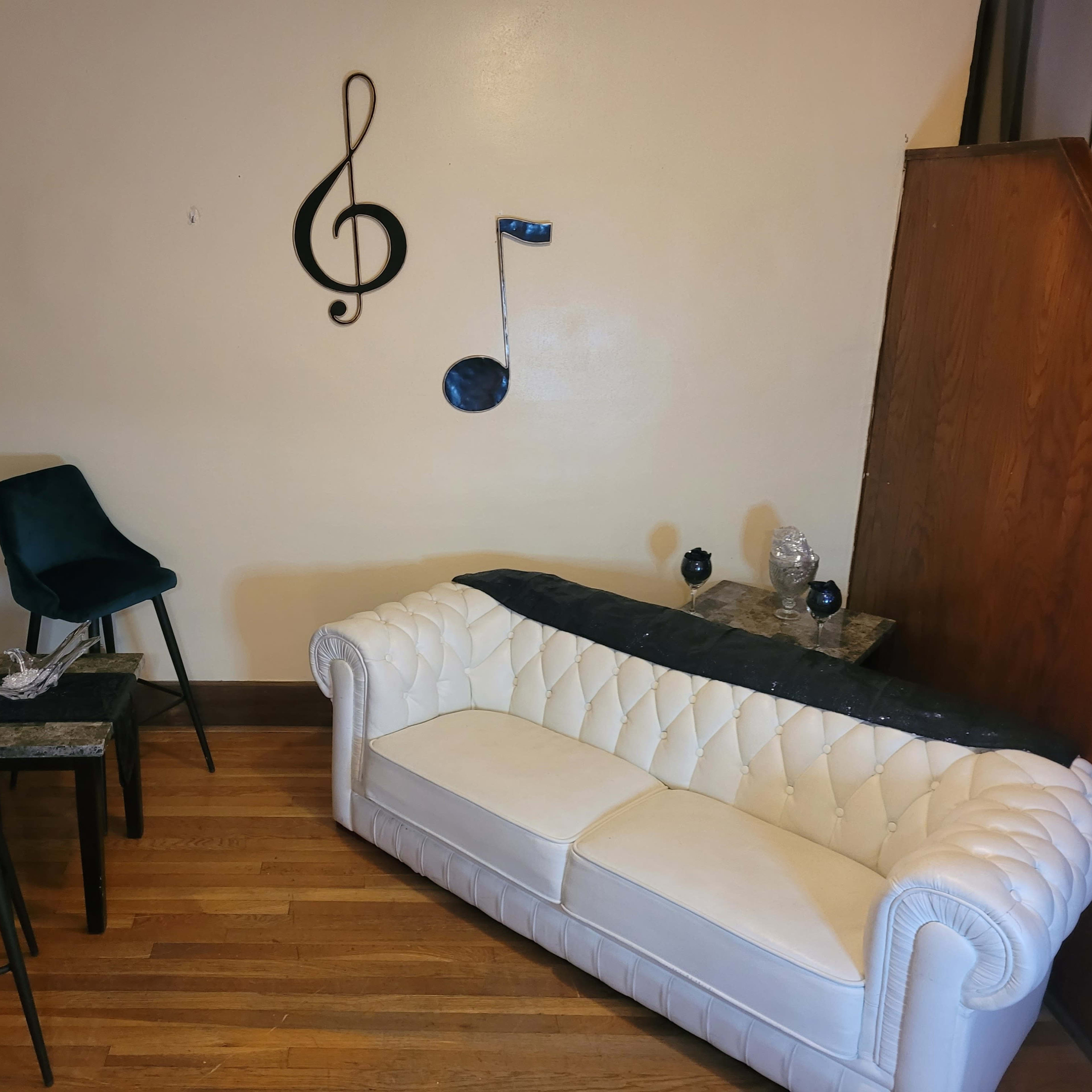 The room features a white tufted sofa, a small table with two dark chairs, and musical note decorations on the wall.
