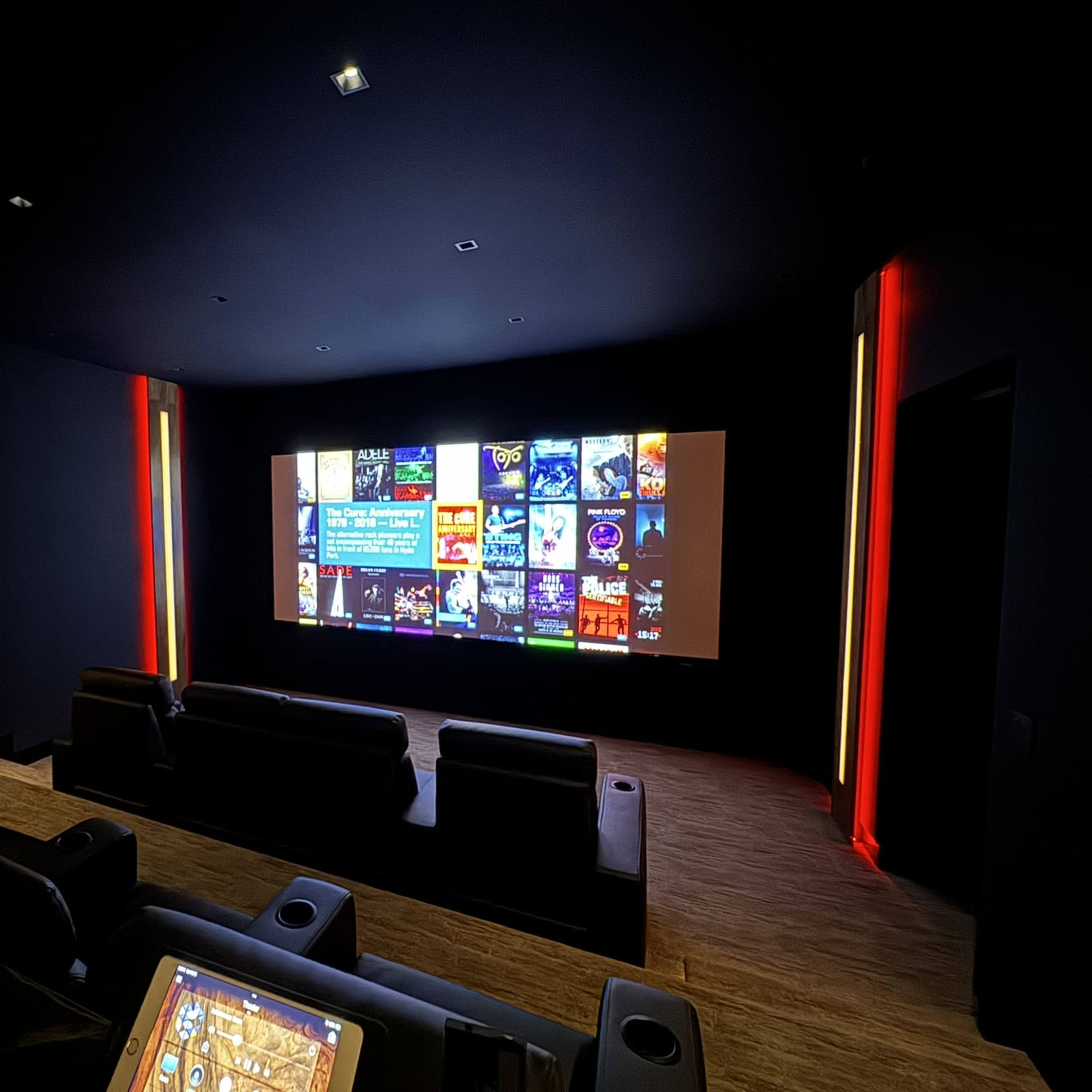 A darkened home theater with black leather seating and a large screen displaying various movie and show options.