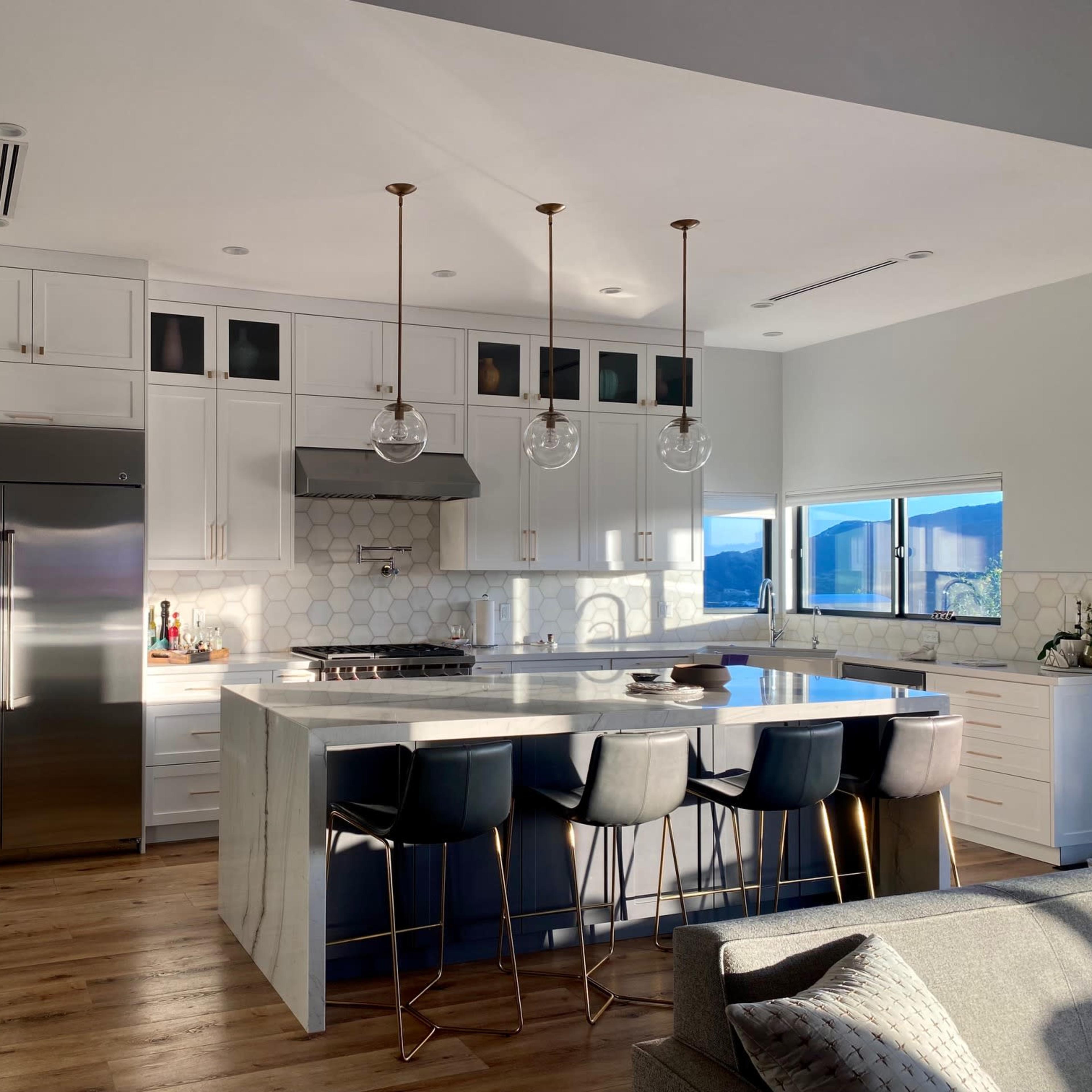 A modern kitchen features white cabinetry, a large central island with bar seating, and stainless steel appliances.