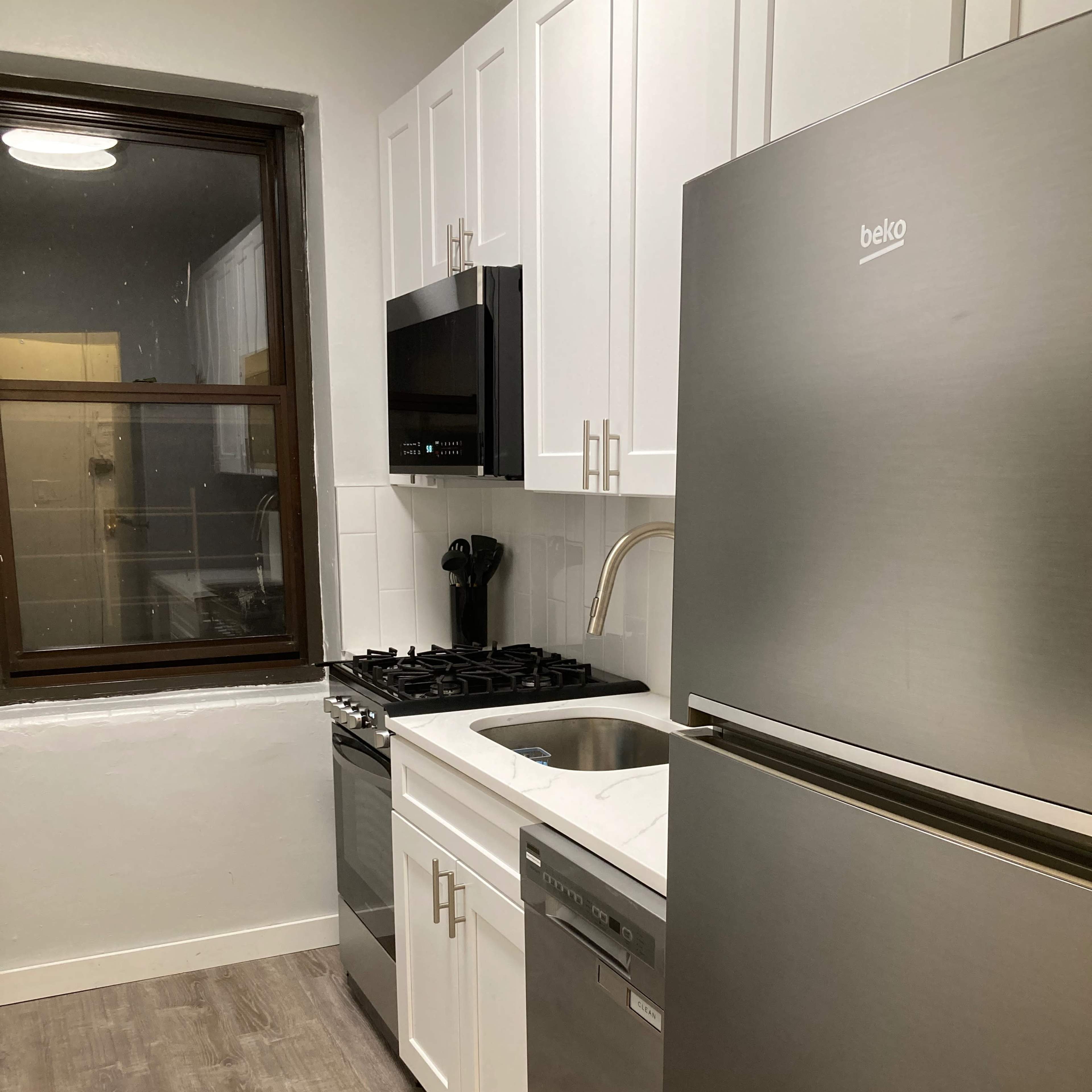 A modern kitchen featuring white cabinetry, a stainless steel refrigerator, a gas stove, and a dishwasher along with a window above the sink.
