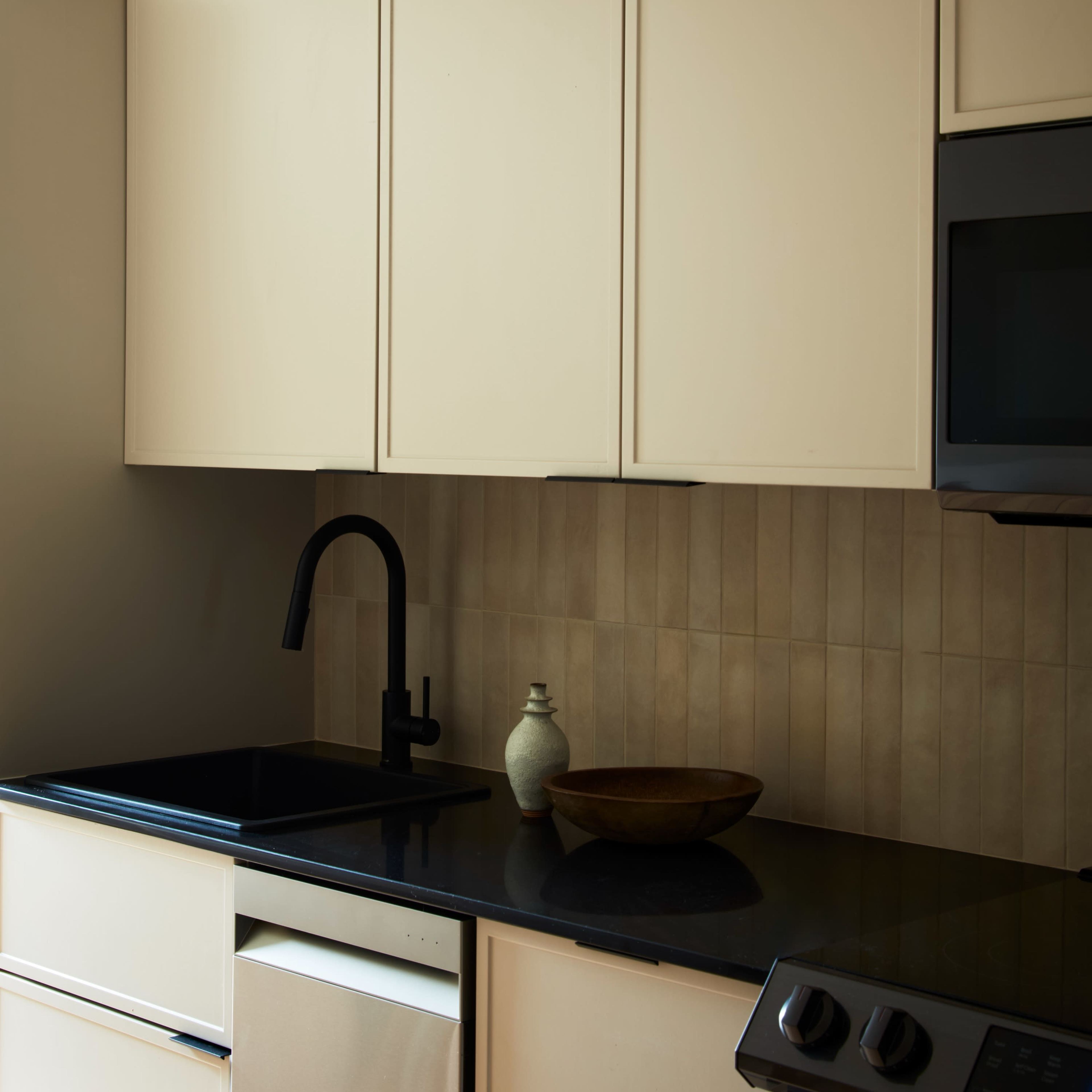 A minimalist kitchen featuring cream-colored cabinets, a black countertop, and a modern faucet.