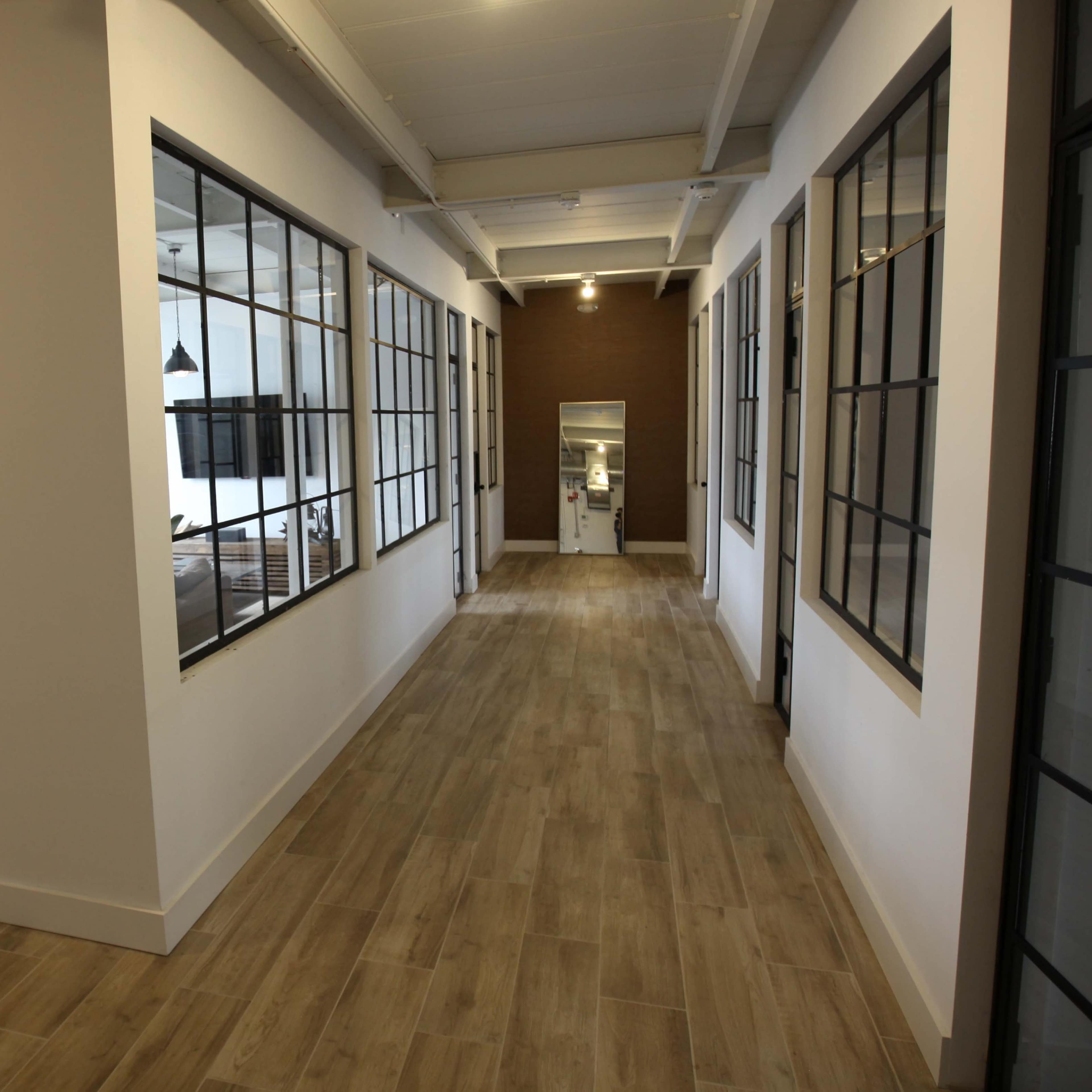 A hallway with large glass-paneled walls on either side, leading to a room at the end.