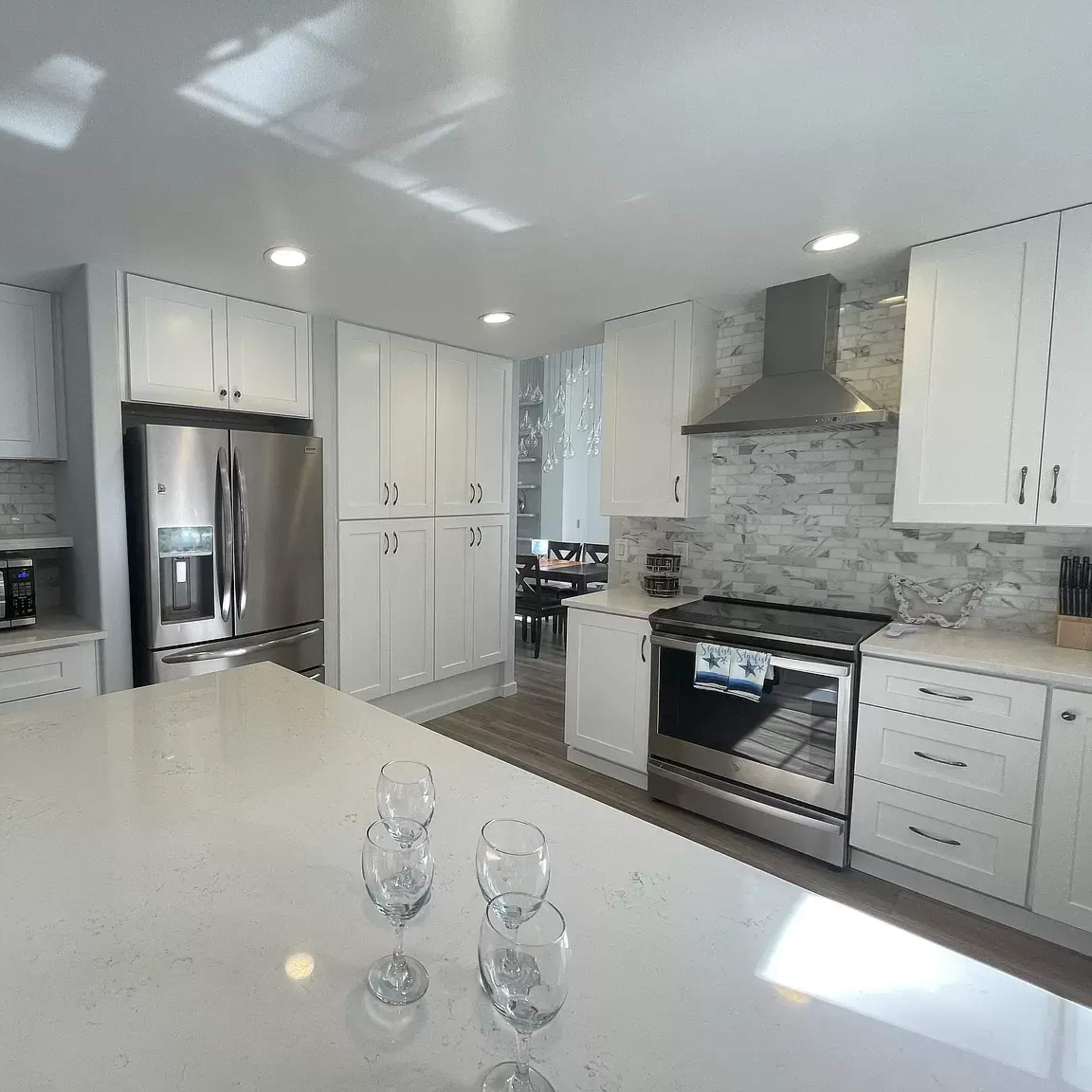 A modern kitchen featuring white cabinets, stainless steel appliances, and a large island with three glasses on it.