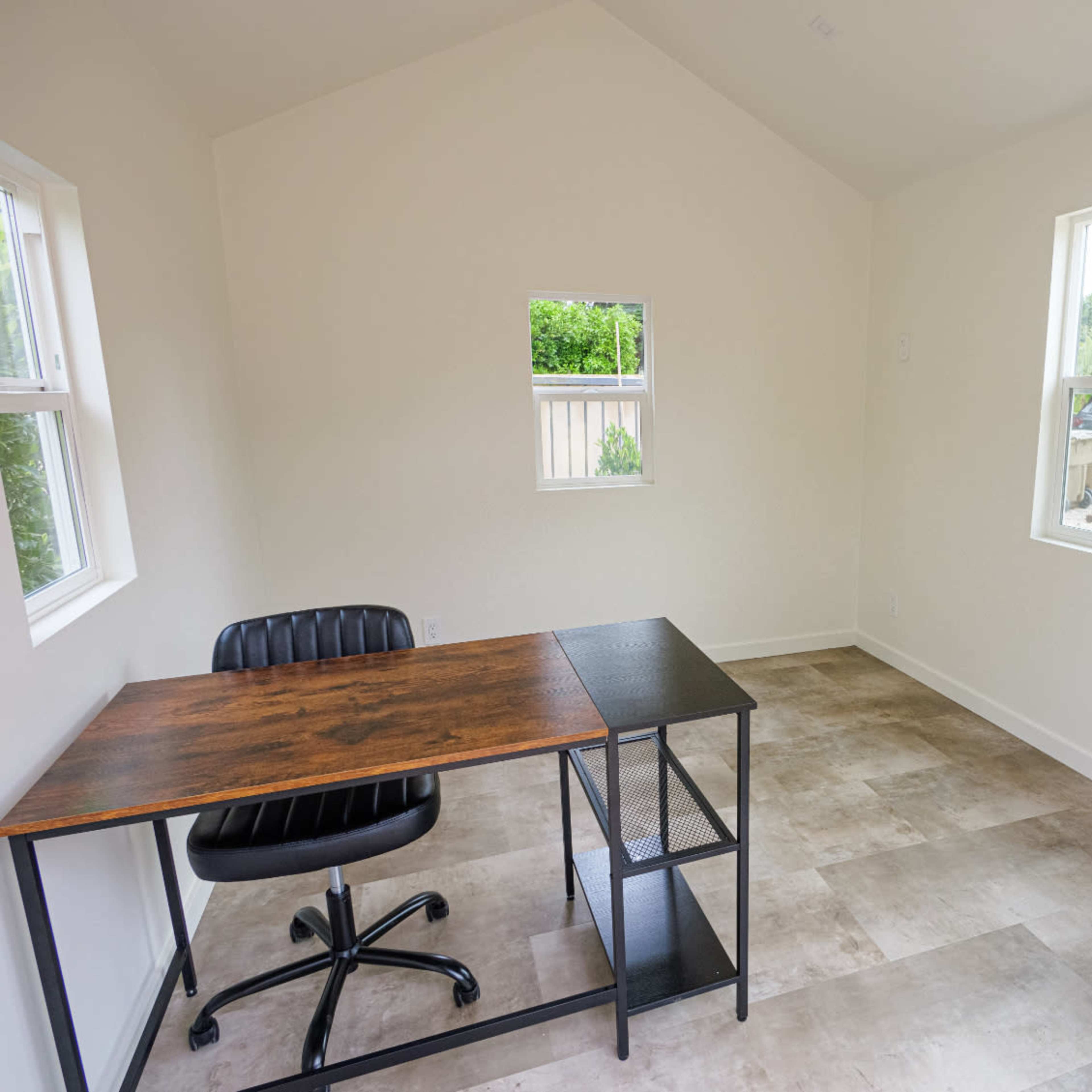 A small, empty room features a desk with a chair, two windows, and a couch.