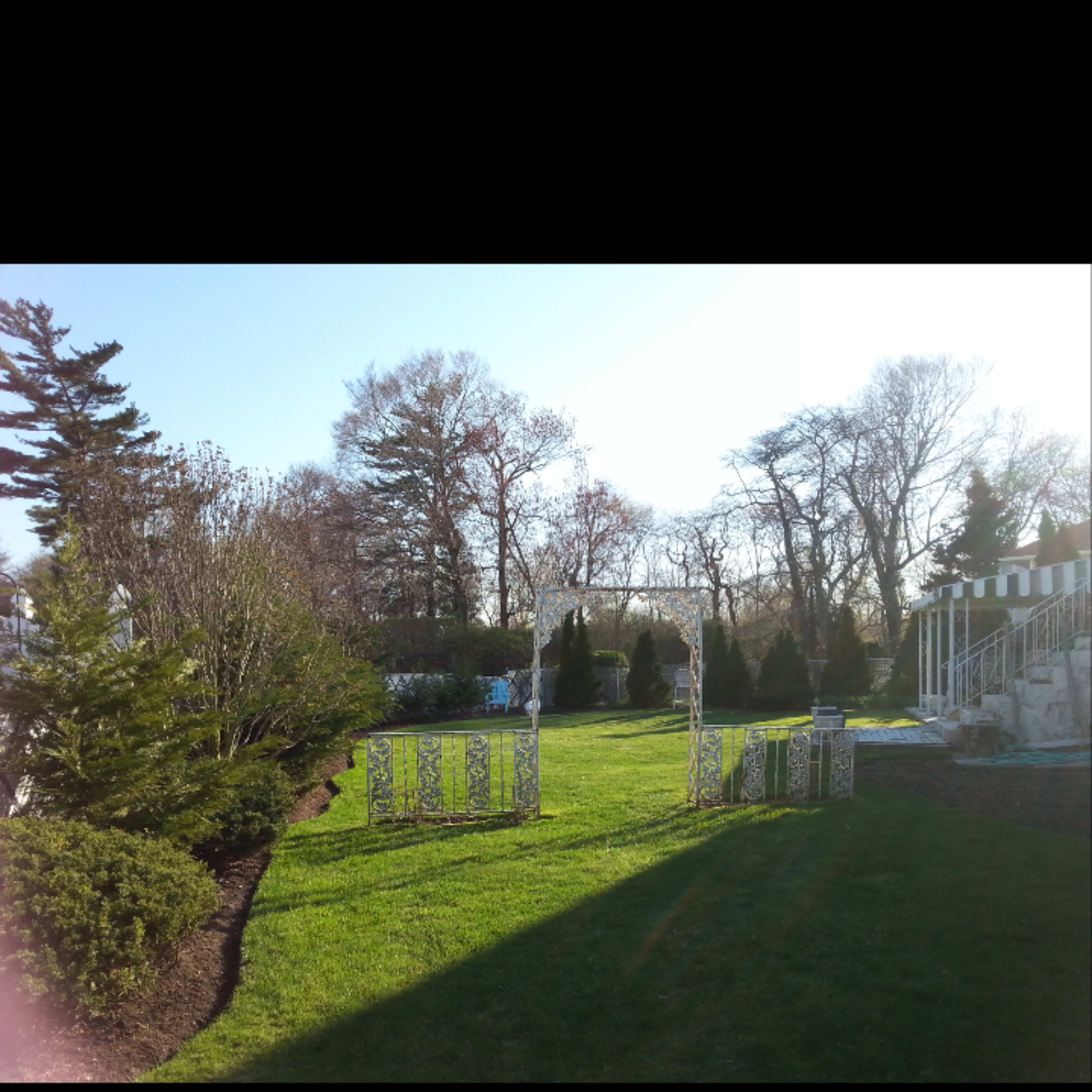 A landscaped garden with green grass, trees in the background, and a white trellis at the edge of the lawn.