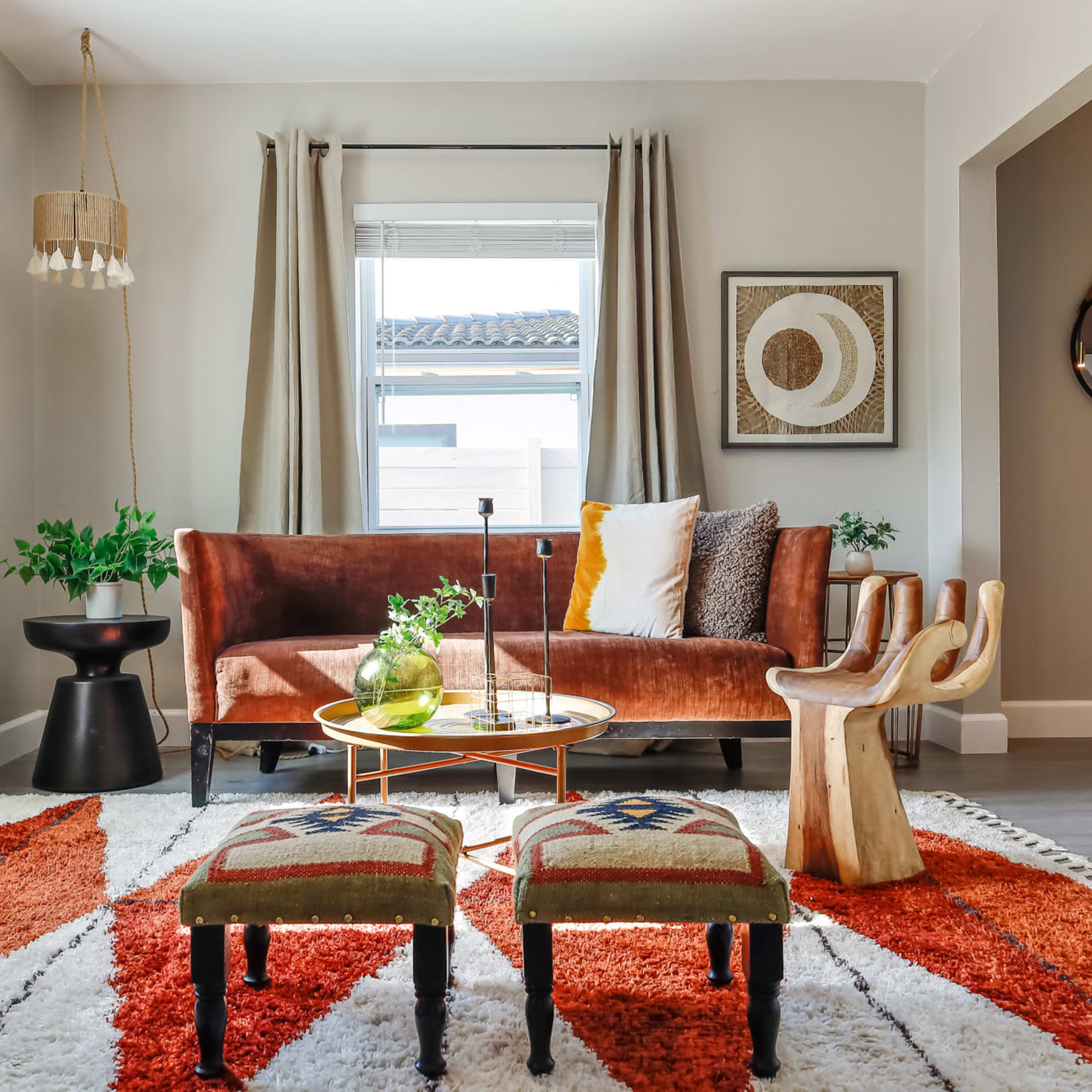A cozy living room features a brown velvet sofa, a round coffee table, decorative stools, and a patterned area rug.