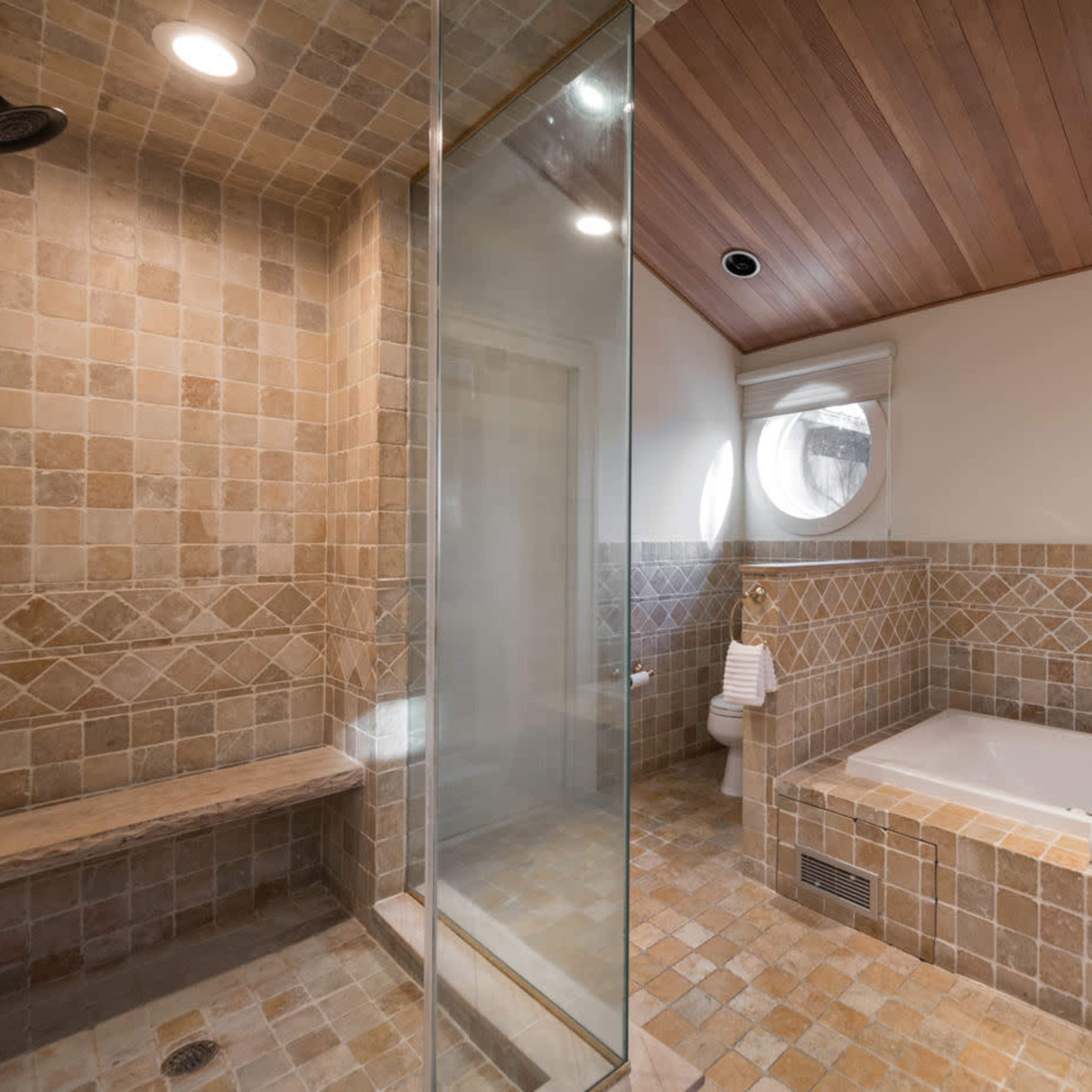A modern bathroom with a glass shower, a tiled bathtub enclosure, and wooden ceiling accents.