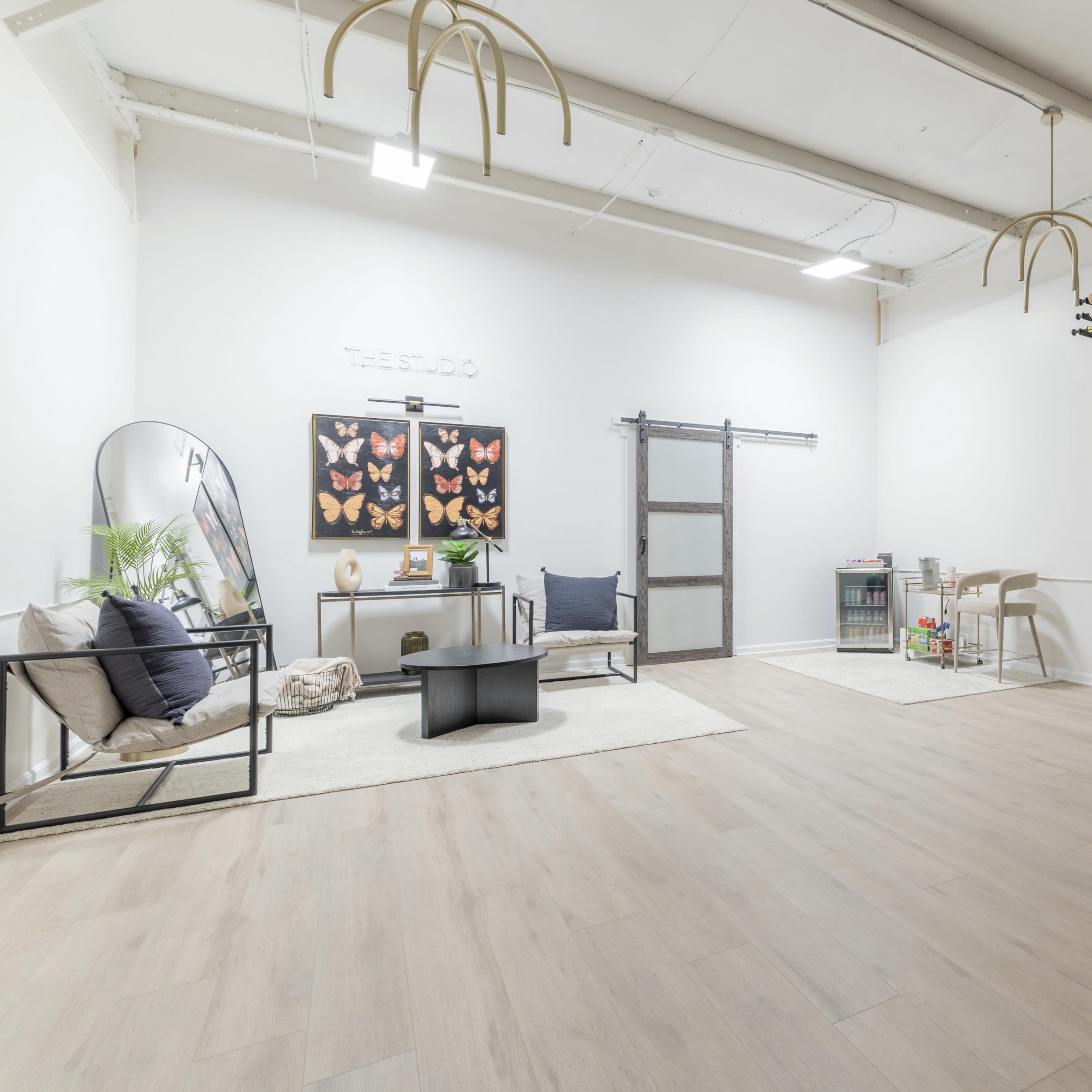 A modern, minimalist studio space with wooden flooring, a seating area, and large decorative wall art featuring butterflies.