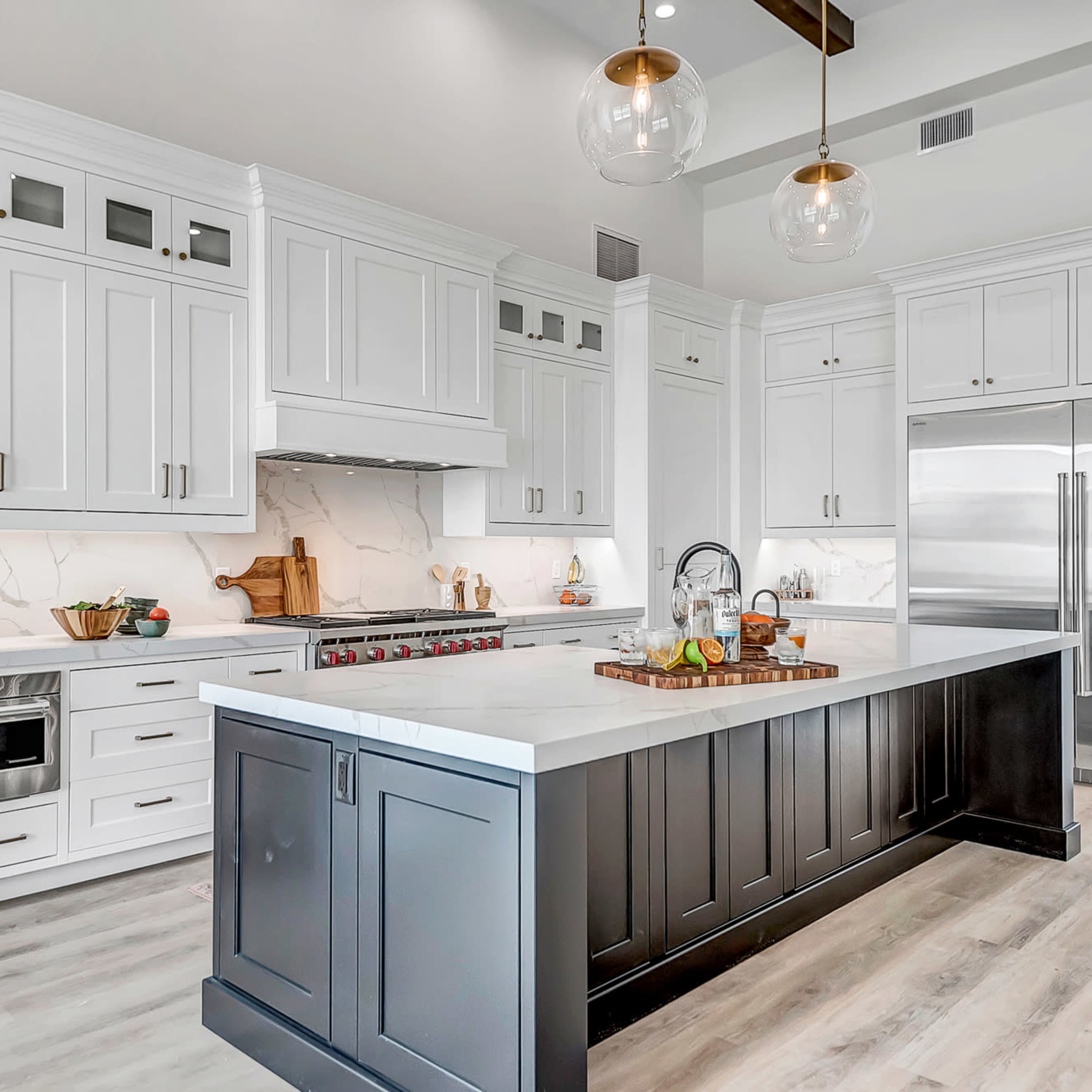 A modern kitchen with white cabinets, a large central island with a dark base, and stainless steel appliances.
