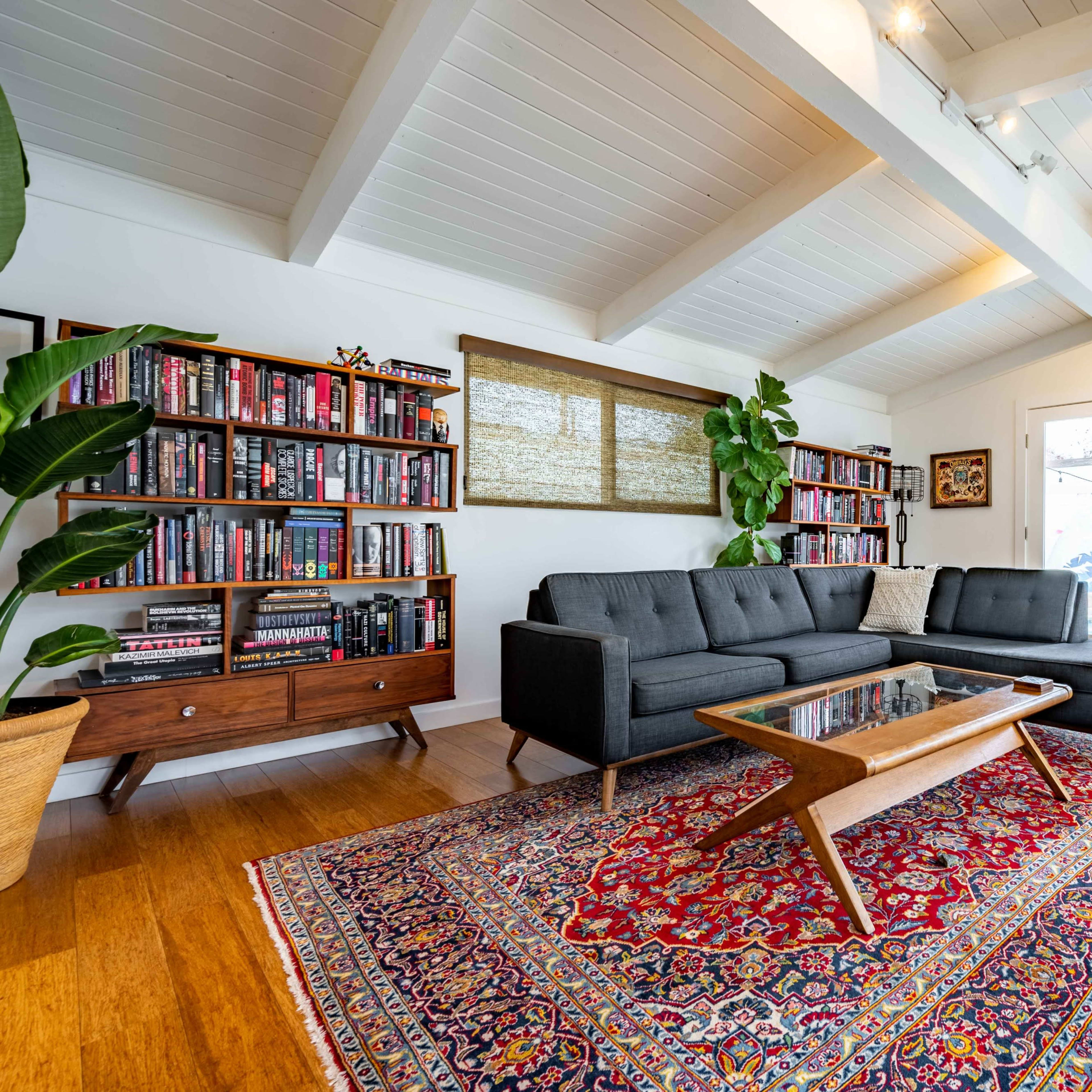 A modern living room with a sectional sofa, a coffee table, bookshelves filled with books, and a children's teepee in the corner.