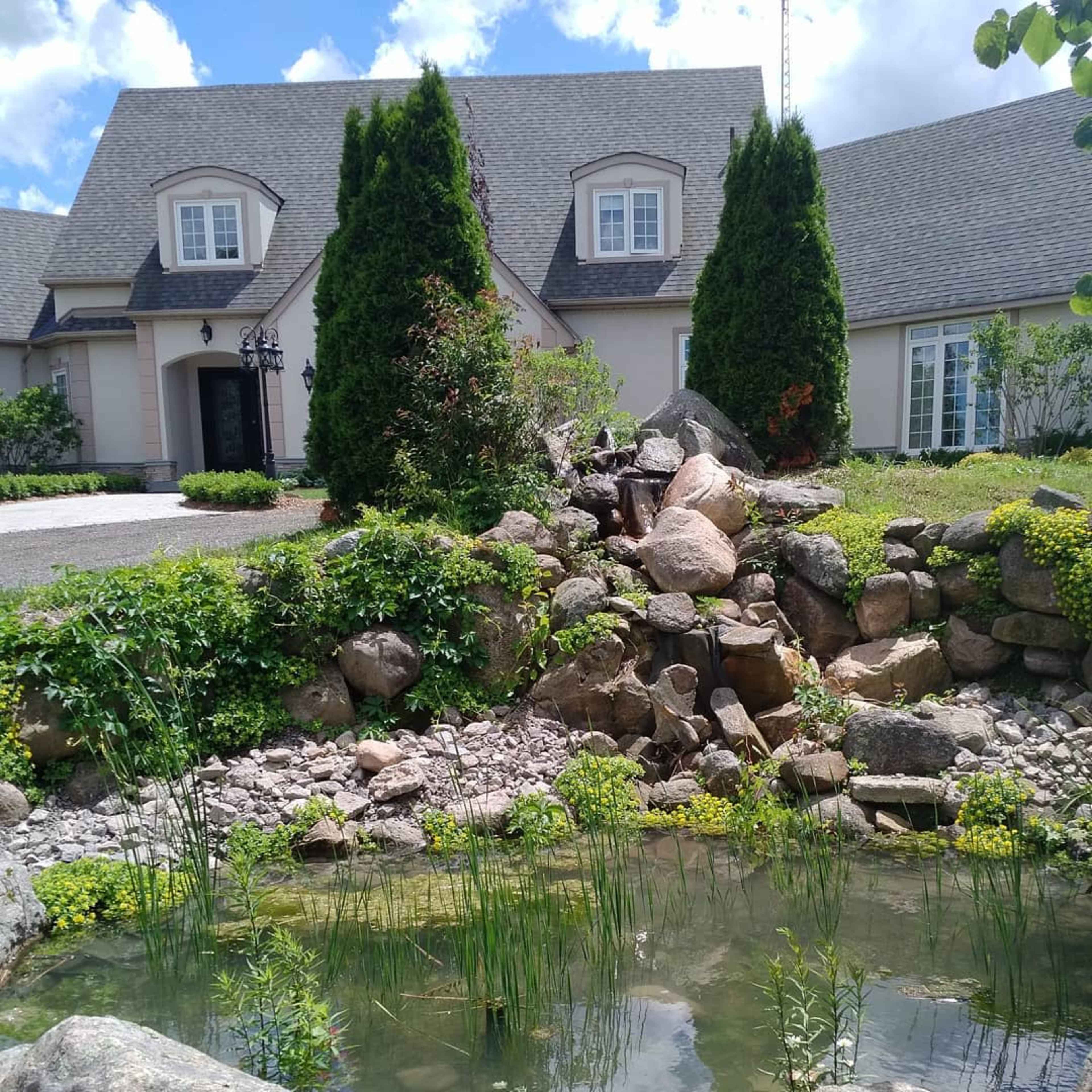 A landscaped front yard with a pond, a rock formation, and a home in the background.