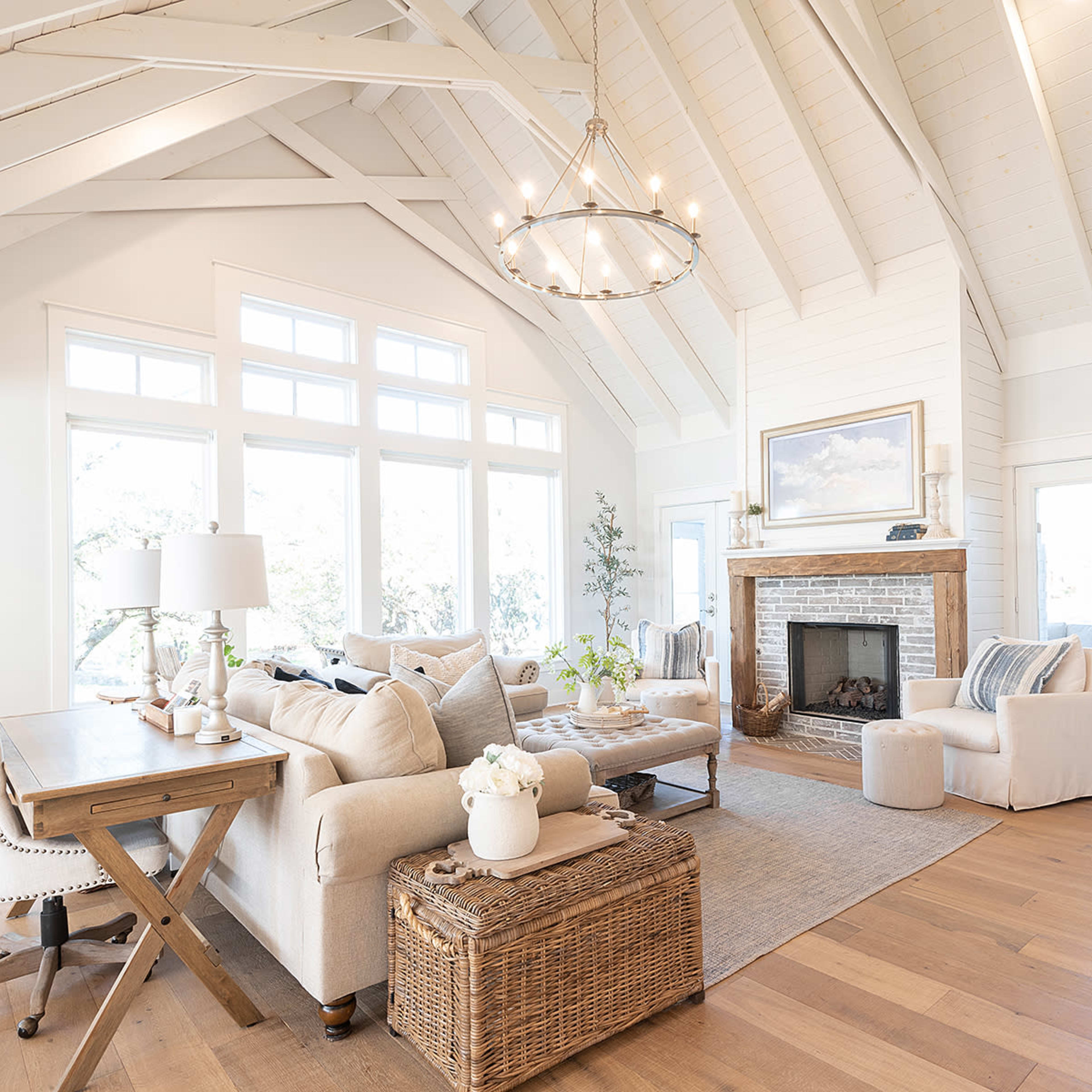 A spacious living room featuring a high vaulted ceiling, a stone fireplace, large windows, and a mix of cozy furniture arranged around a central area.