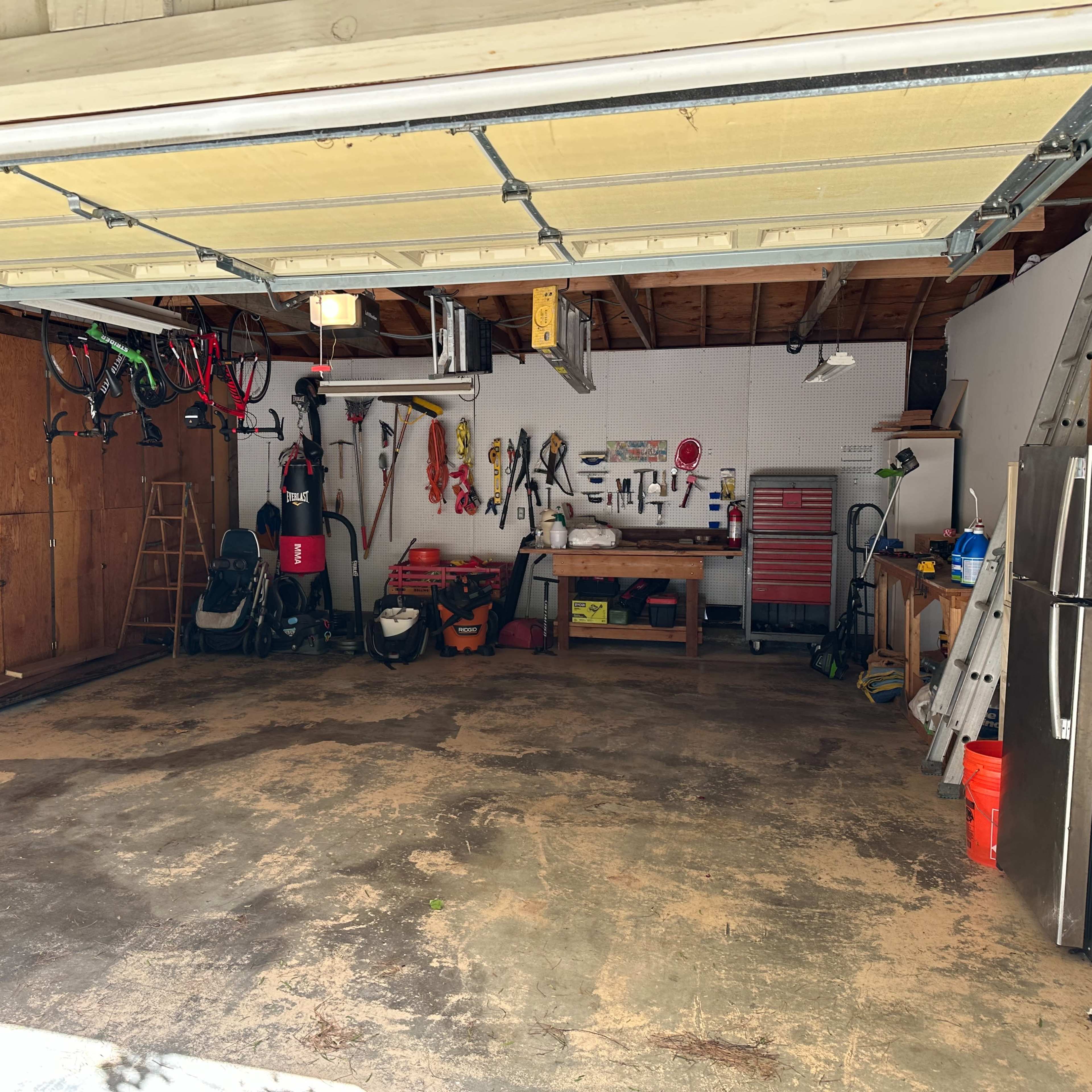 A spacious garage with exposed wooden beams, various tools and equipment hanging on the walls, and a clean, open floor.