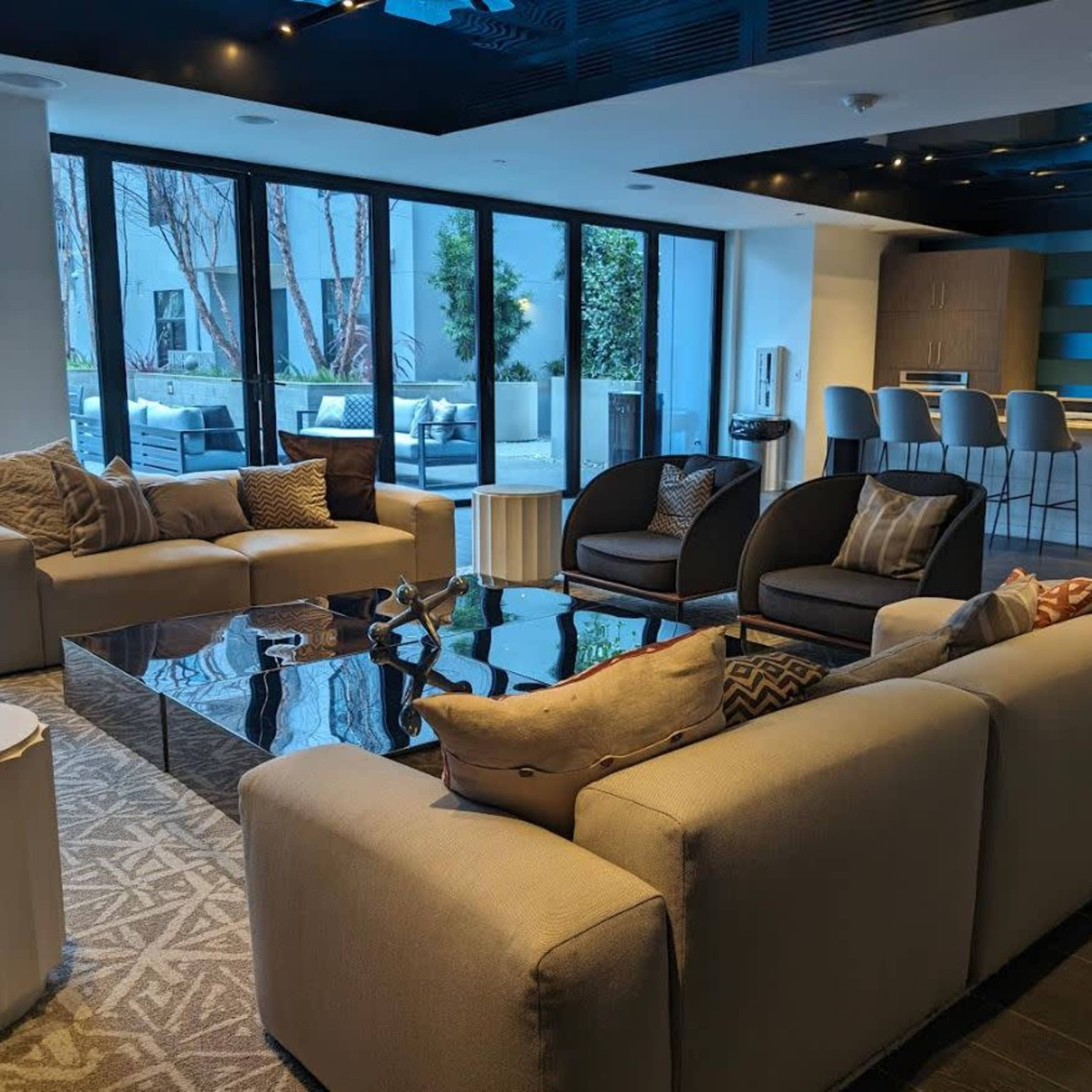 A modern living space with a seating area featuring sofas and chairs, a coffee table, and a view of an outdoor area through large windows.