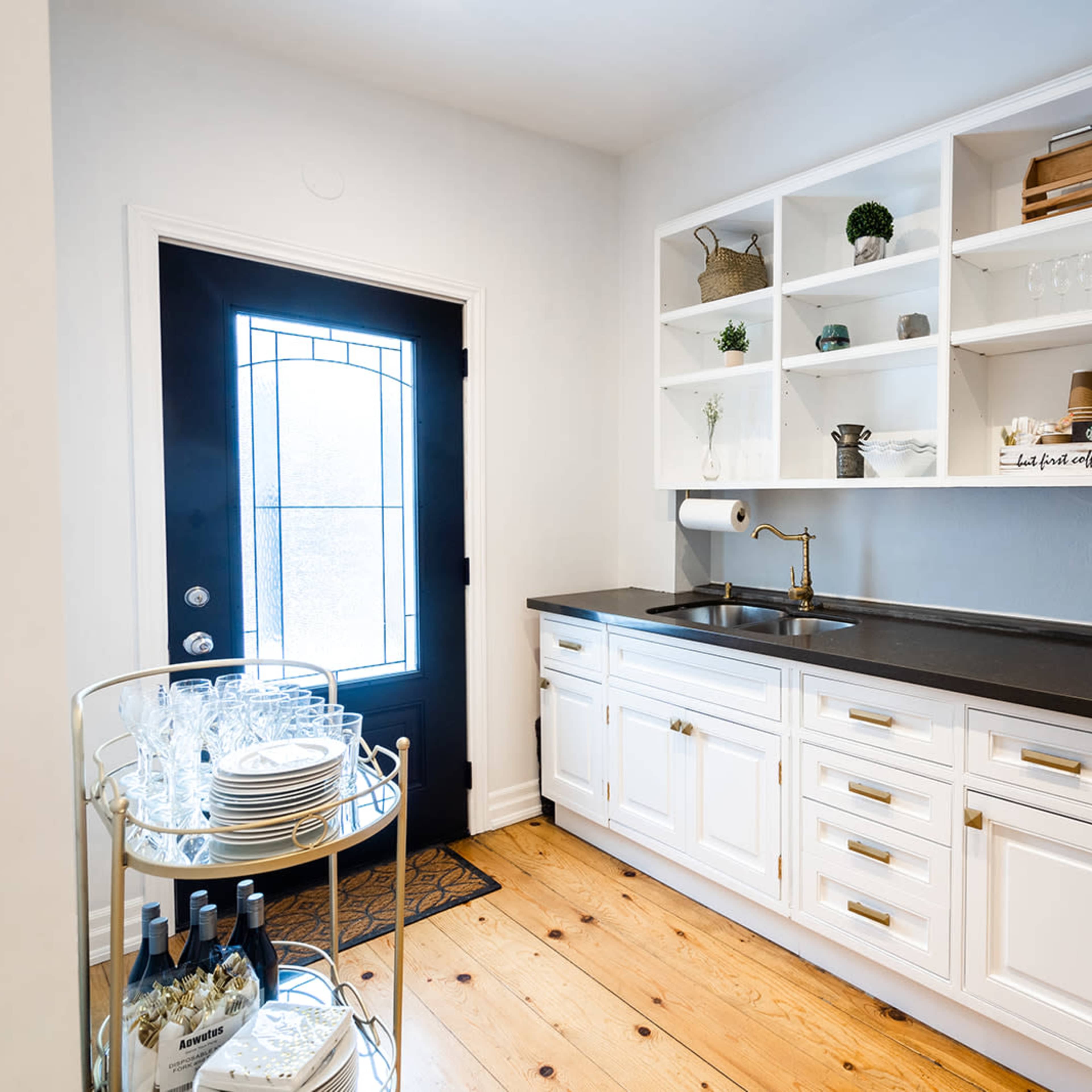 A compact kitchen area with white cabinetry, a black countertop, a sink, and a laundry unit beside a black door, all set against a light-colored wall.