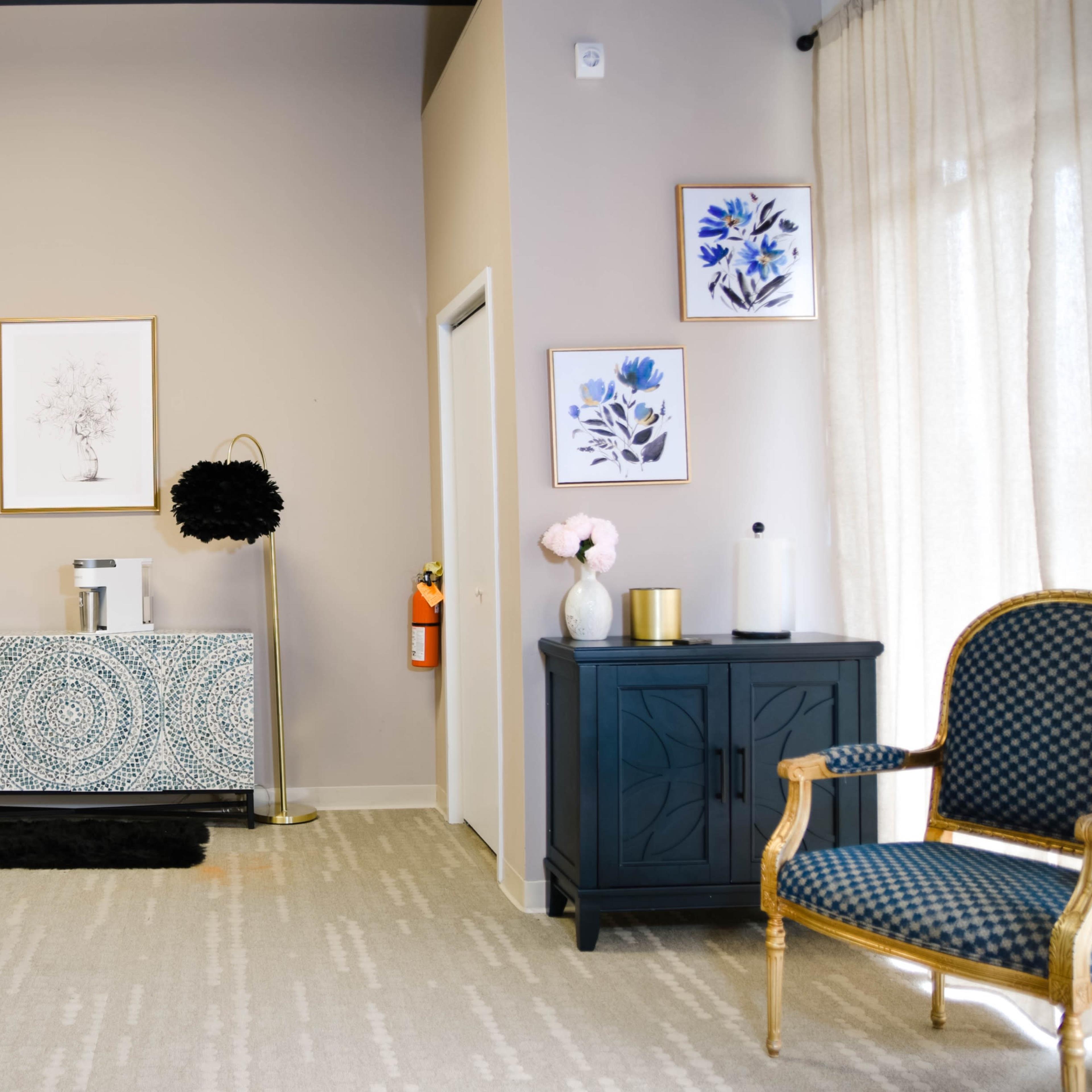 A modern office space featuring a patterned sideboard, a desk with a chair, decorative artwork on the walls, and a plush armchair.