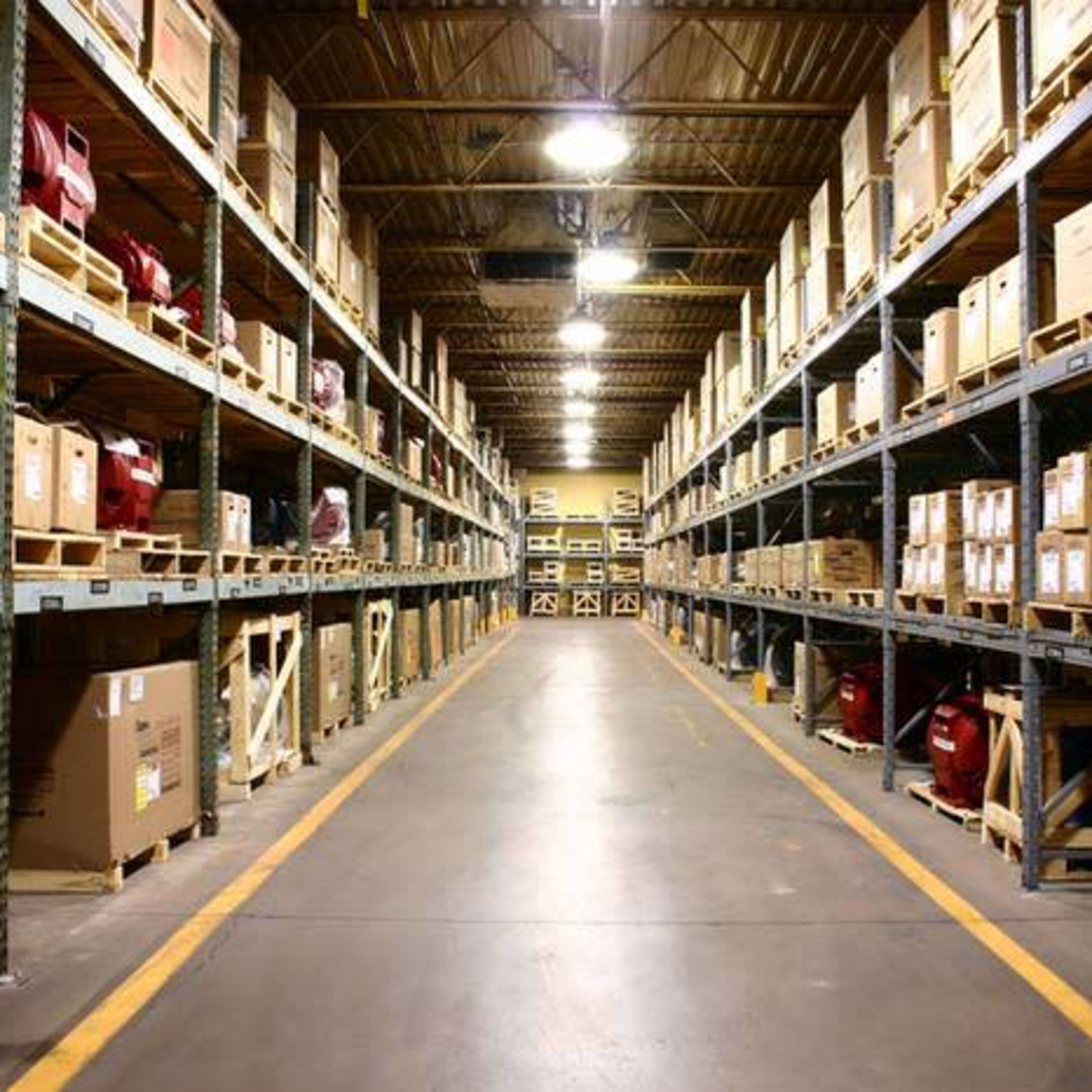 An organized warehouse aisle with shelves stacked high with boxes and equipment on either side.