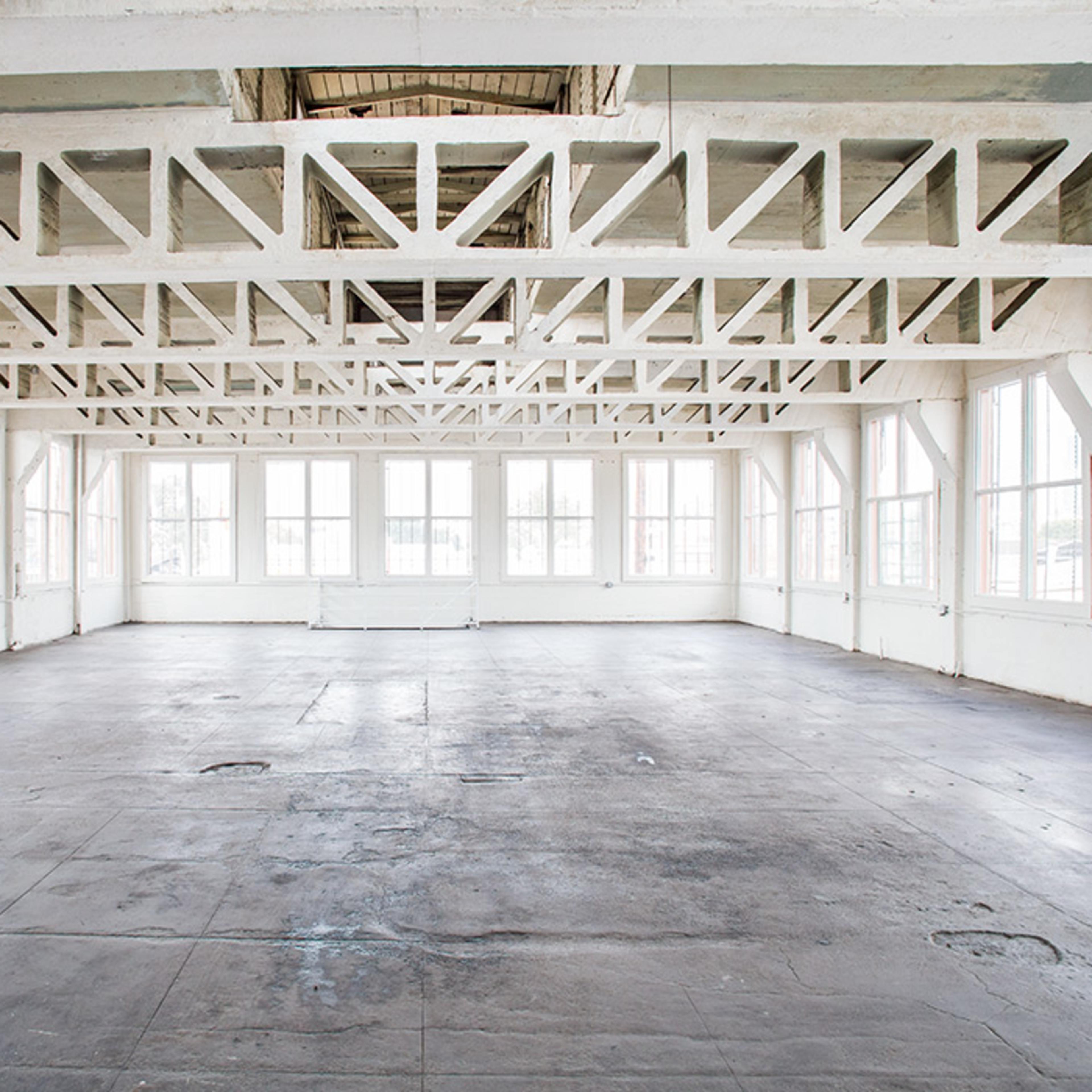 A spacious, empty room with large windows and exposed wooden beams along the ceiling.