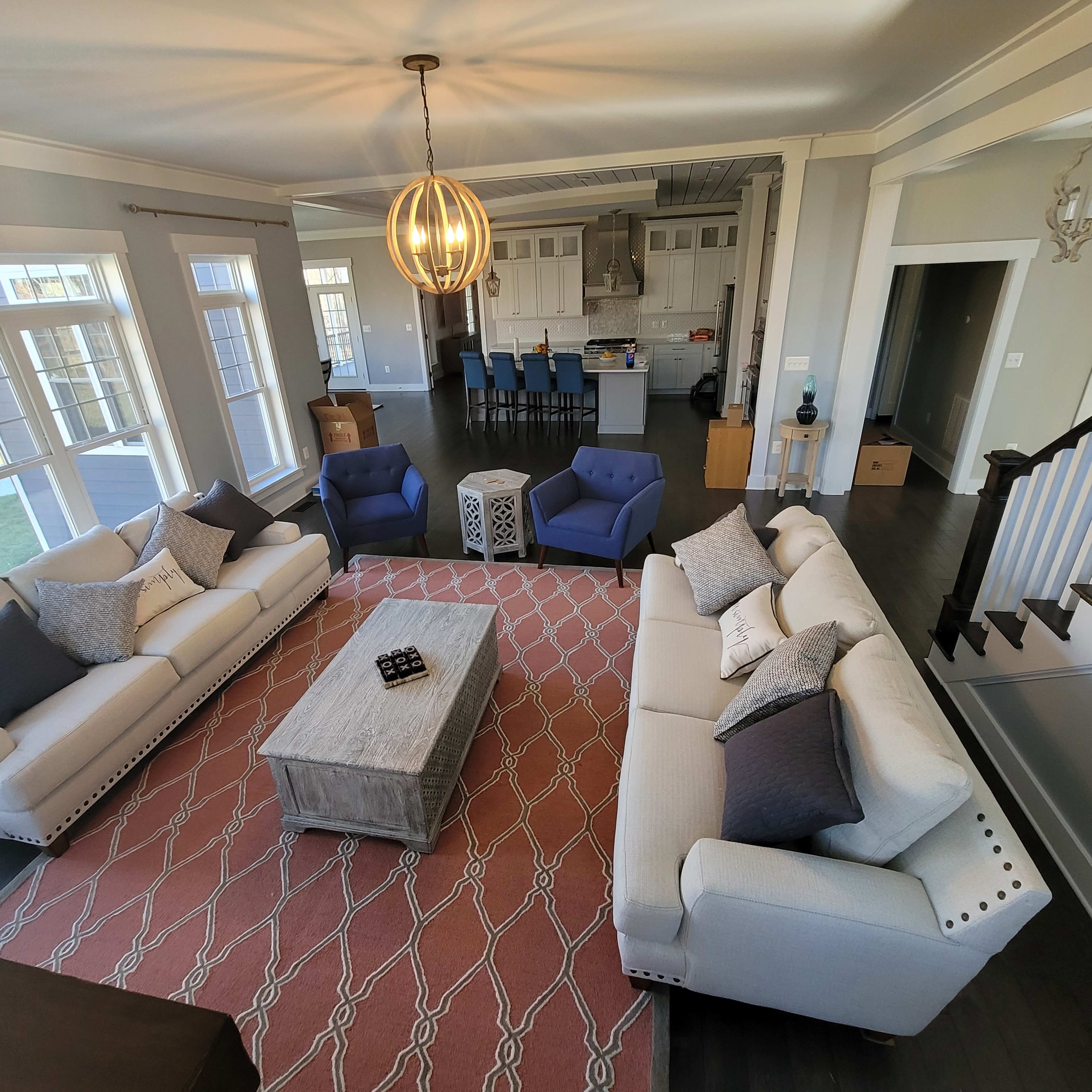 A spacious living area with two sofas, two blue armchairs, a center coffee table, and a patterned rug, leading into an open kitchen.