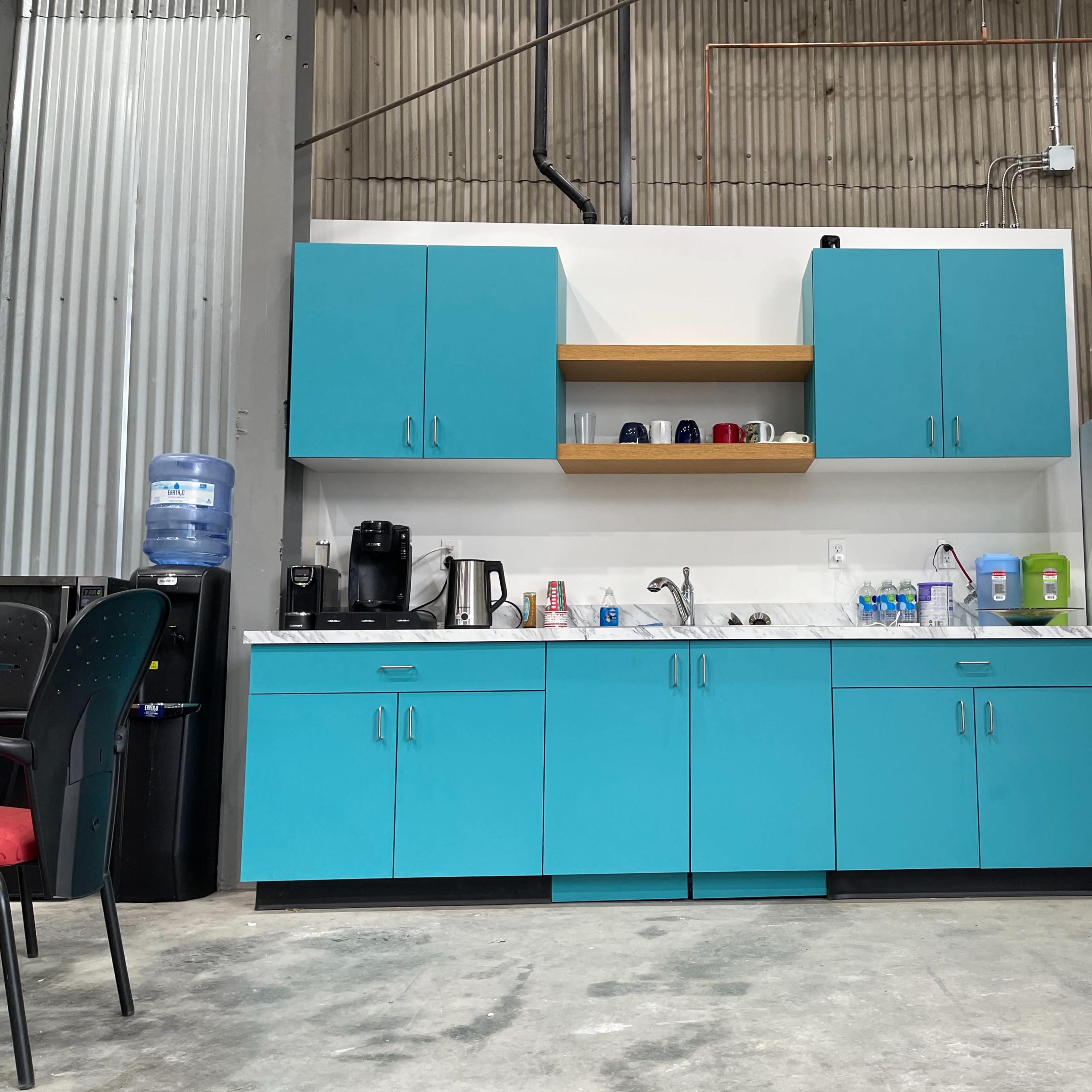 A modern kitchen setup featuring turquoise cabinets, a white refrigerator, and various kitchen appliances on a countertop.