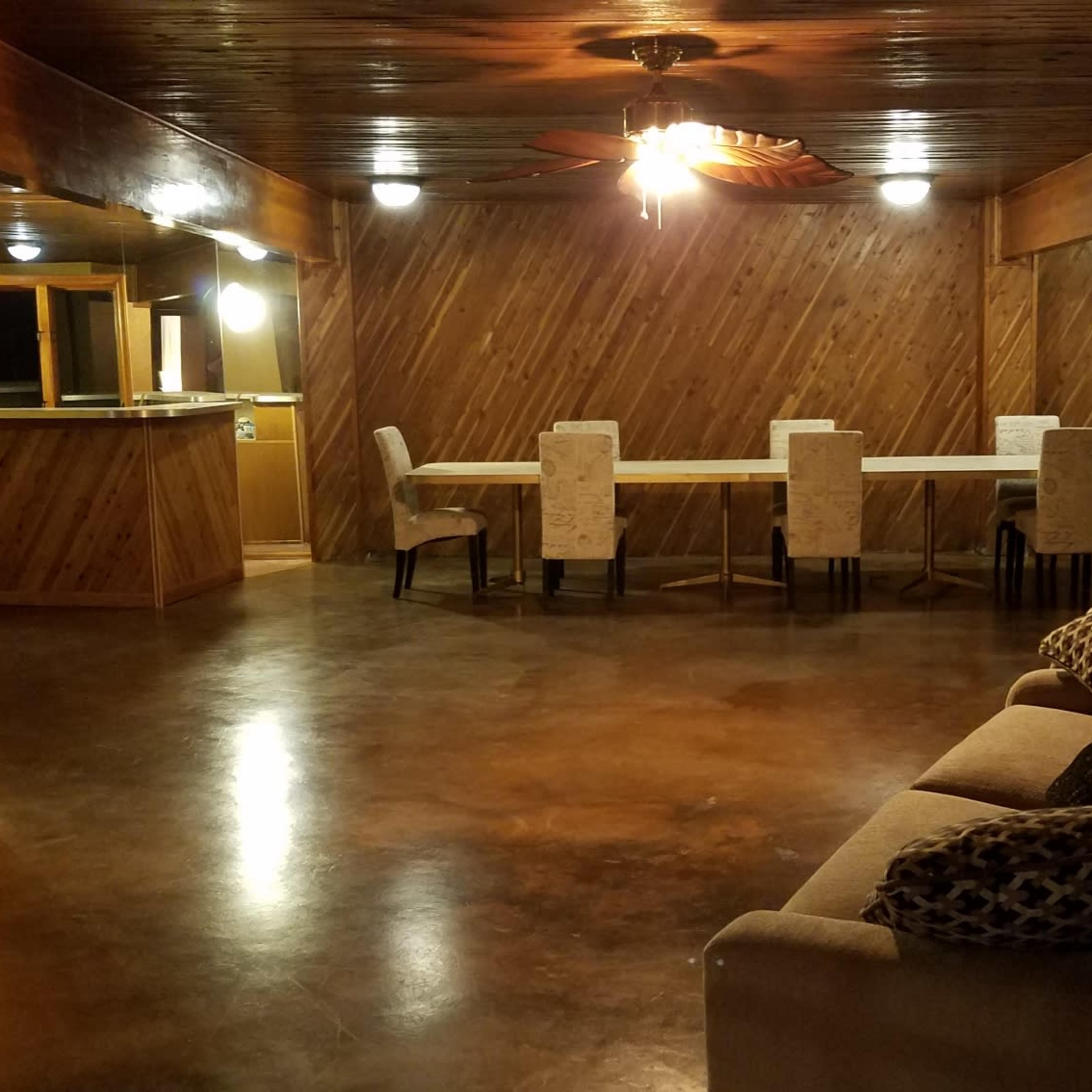 A spacious room features a long table with chairs, a couch along one wall, and wooden paneling on the walls and ceiling.