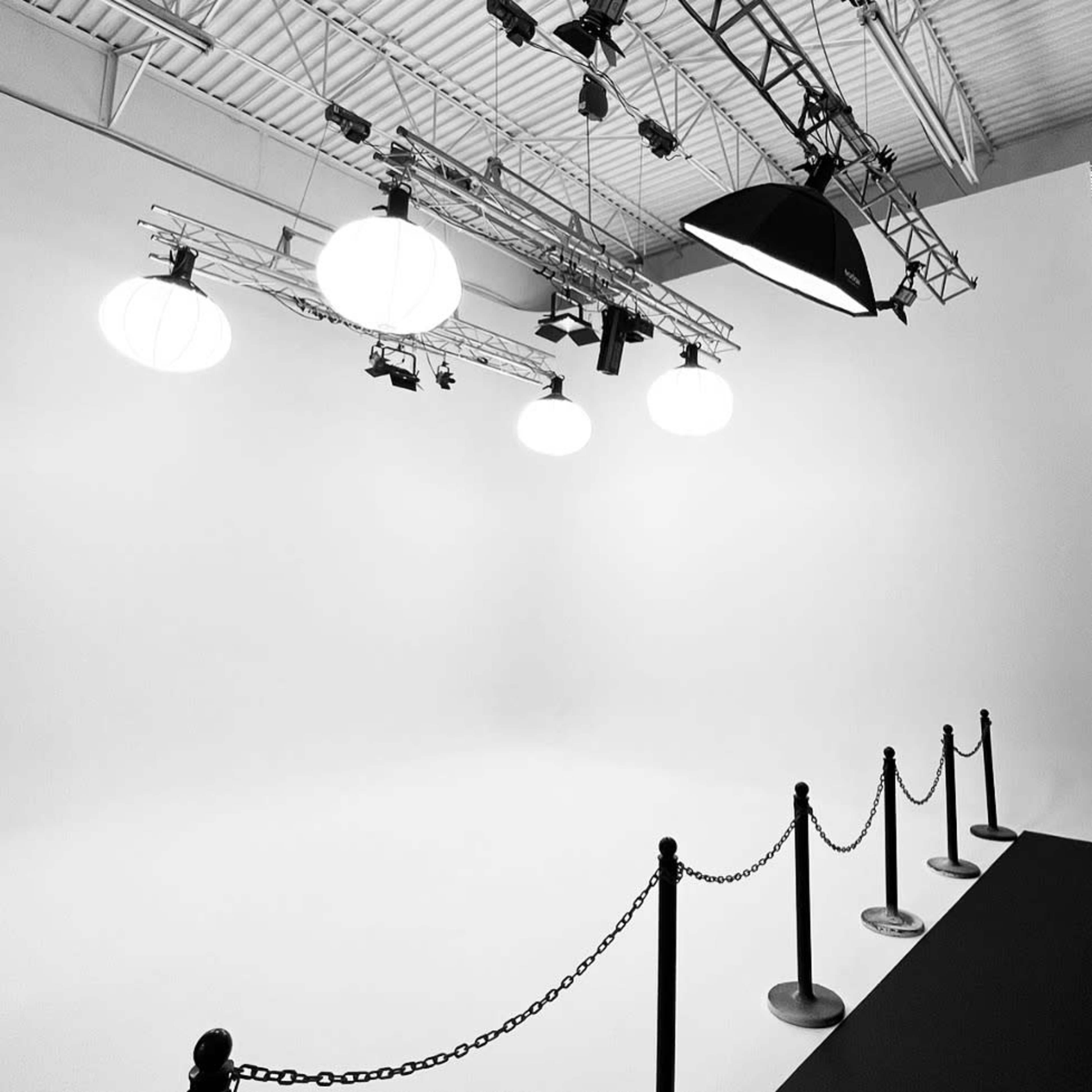 A minimalist studio space with overhead lighting, a black table, and a rope barrier in front of a plain white backdrop.