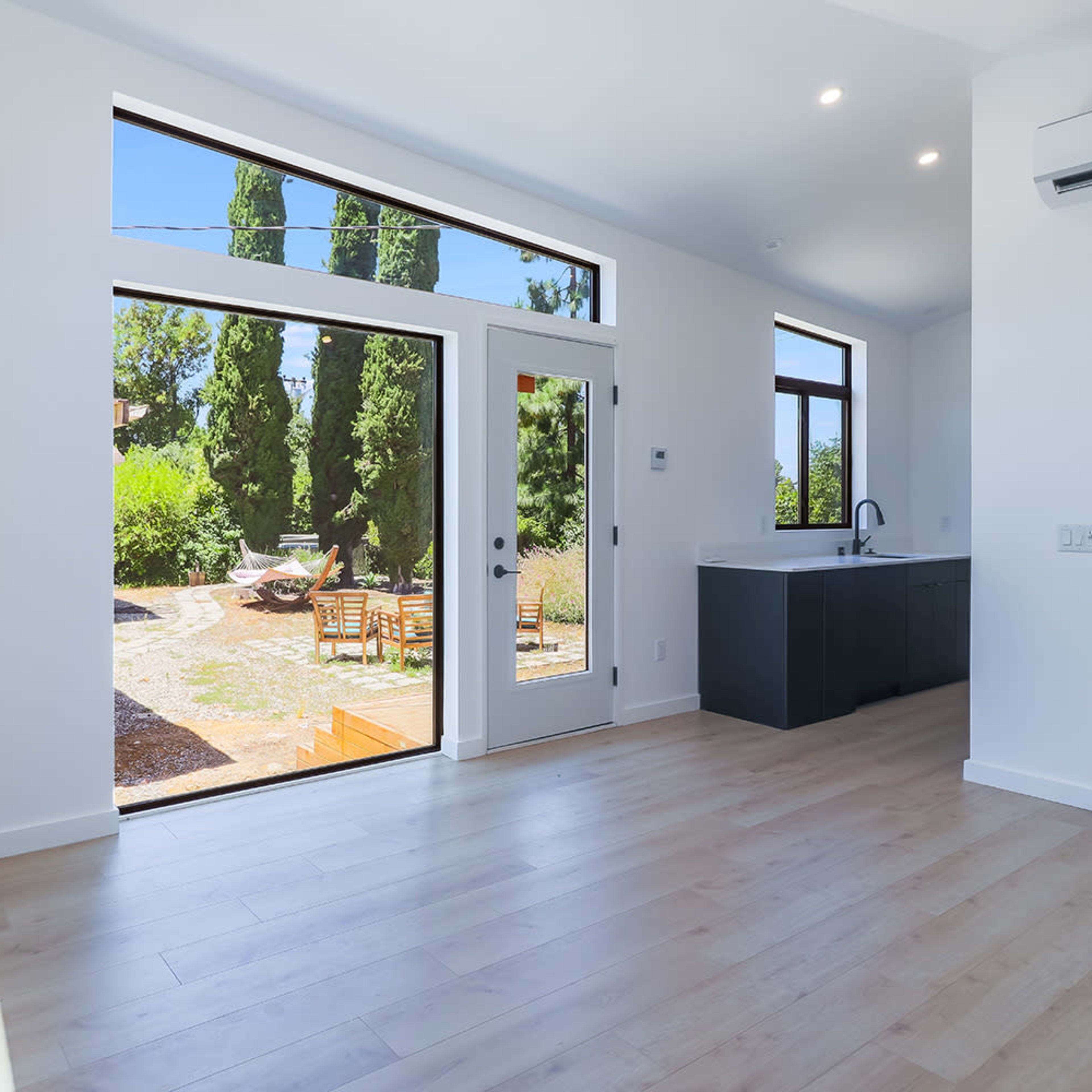 A bright, open interior space with large windows overlooking a landscaped garden and wooden outdoor seating area.