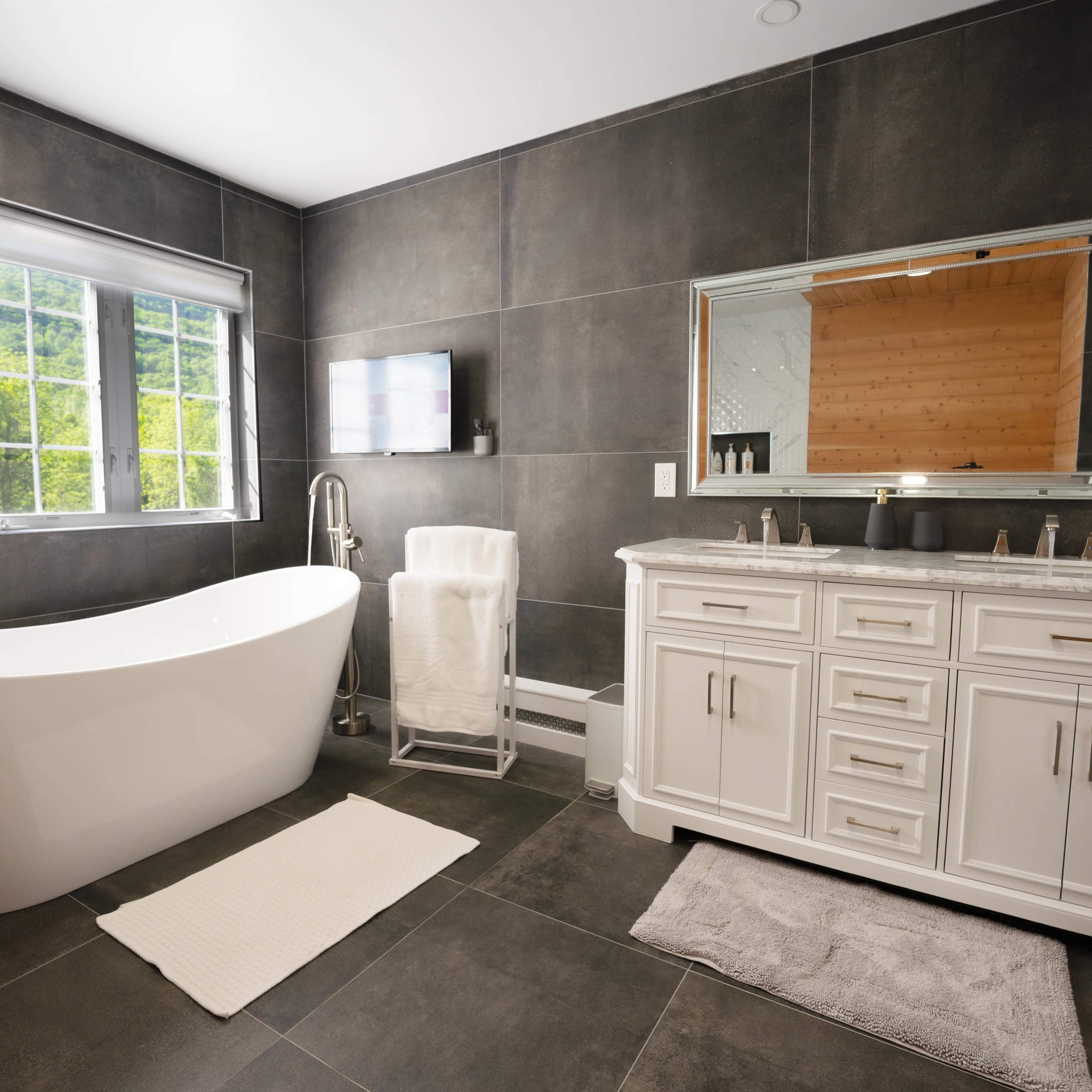 A modern bathroom featuring a freestanding bathtub, a double vanity with a mirror, and a window that lets in natural light.