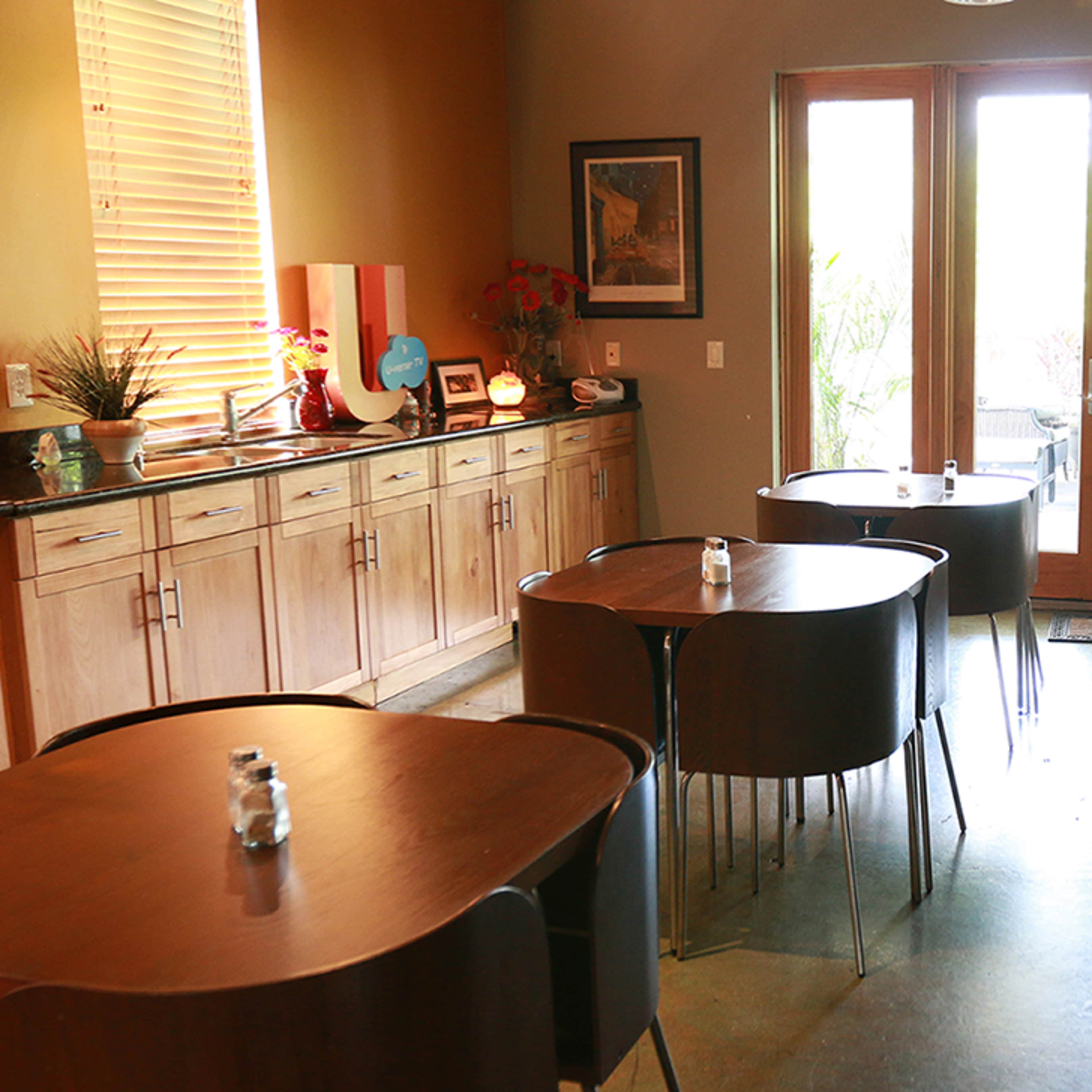 A small café with wooden tables, a countertop area, and large doors leading to an outdoor space.