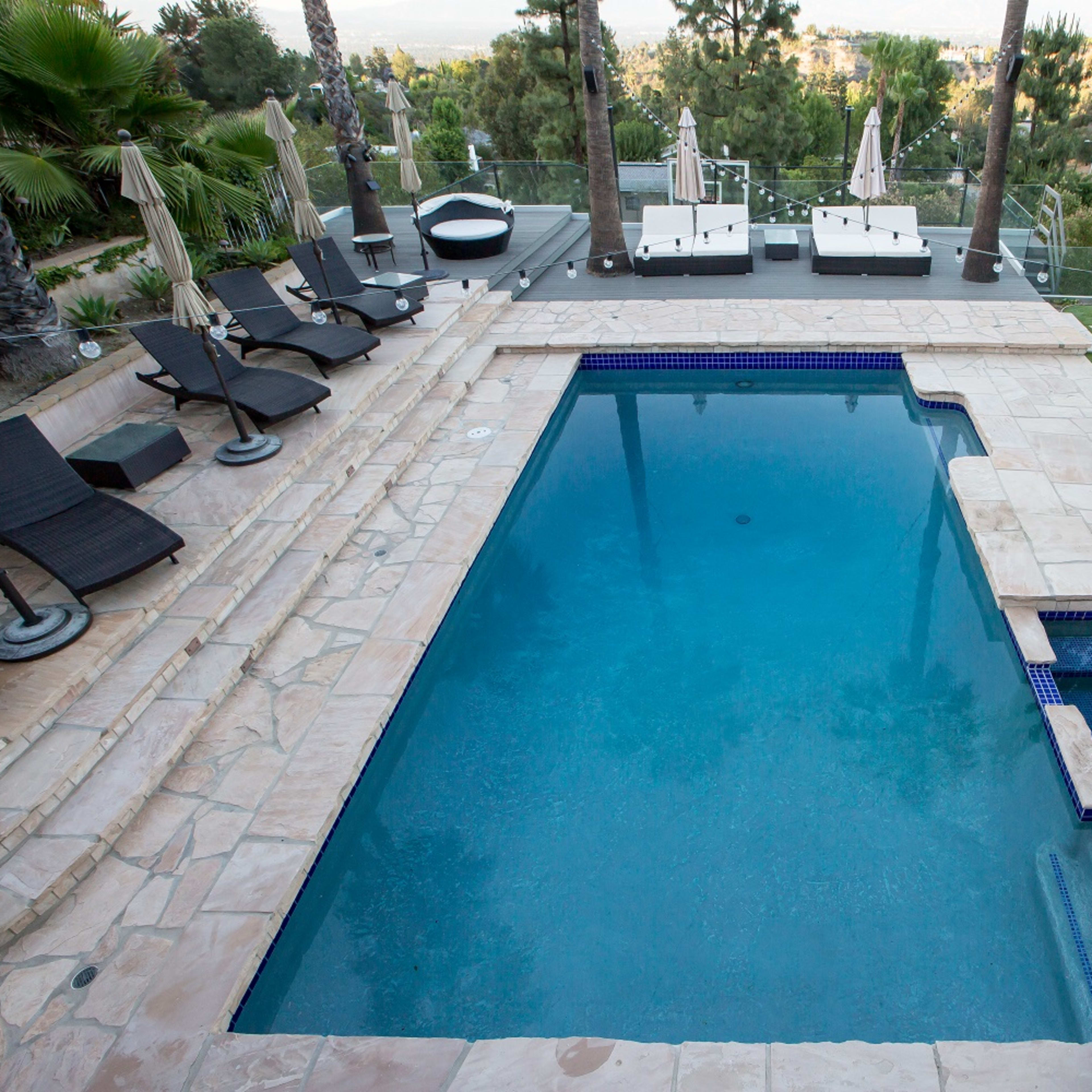 A swimming pool surrounded by lounge chairs and umbrellas, with landscaped greenery in the background.