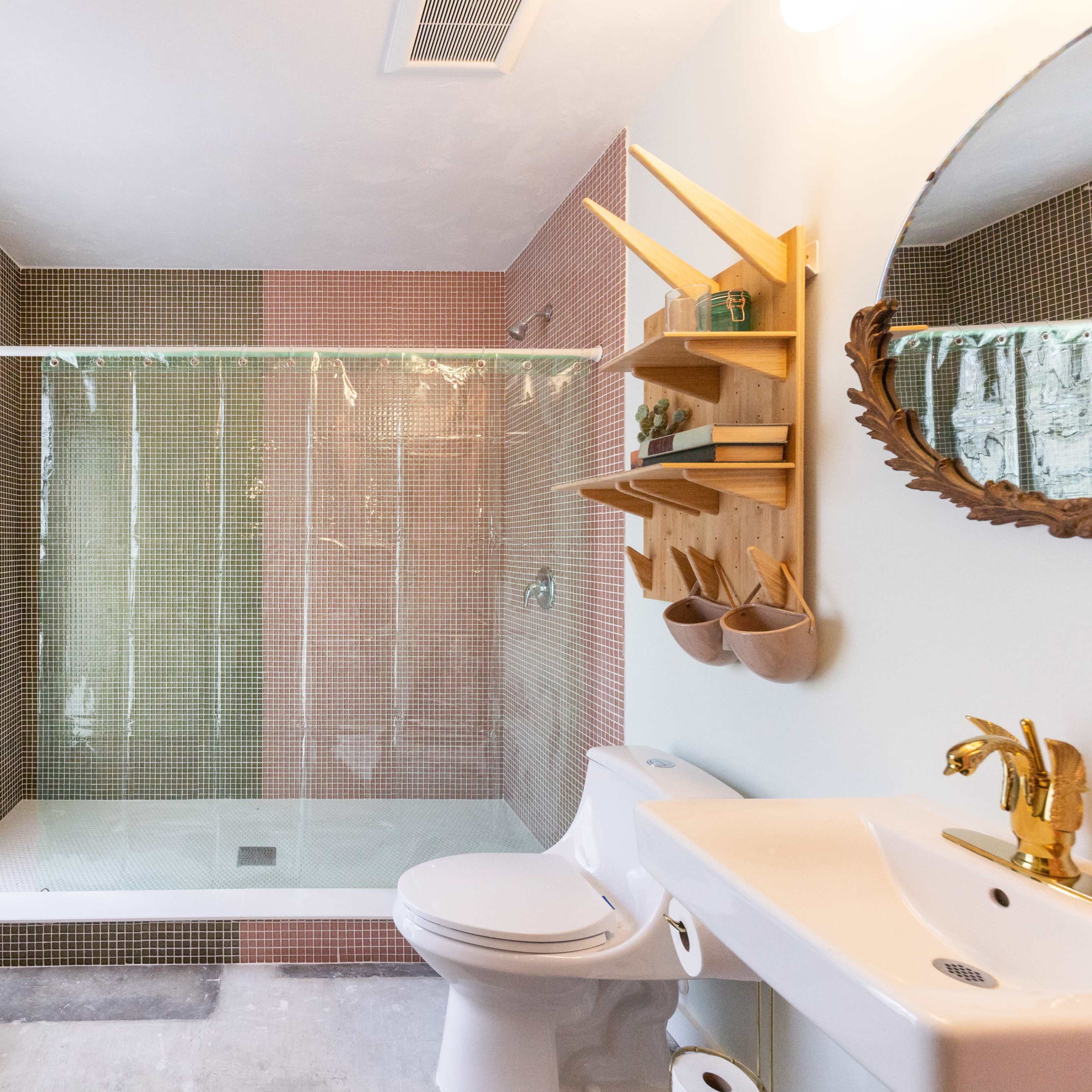 The bathroom features a glass shower enclosed by colorful tiled walls, a compact toilet, and a sink with wooden shelving and decorative elements.