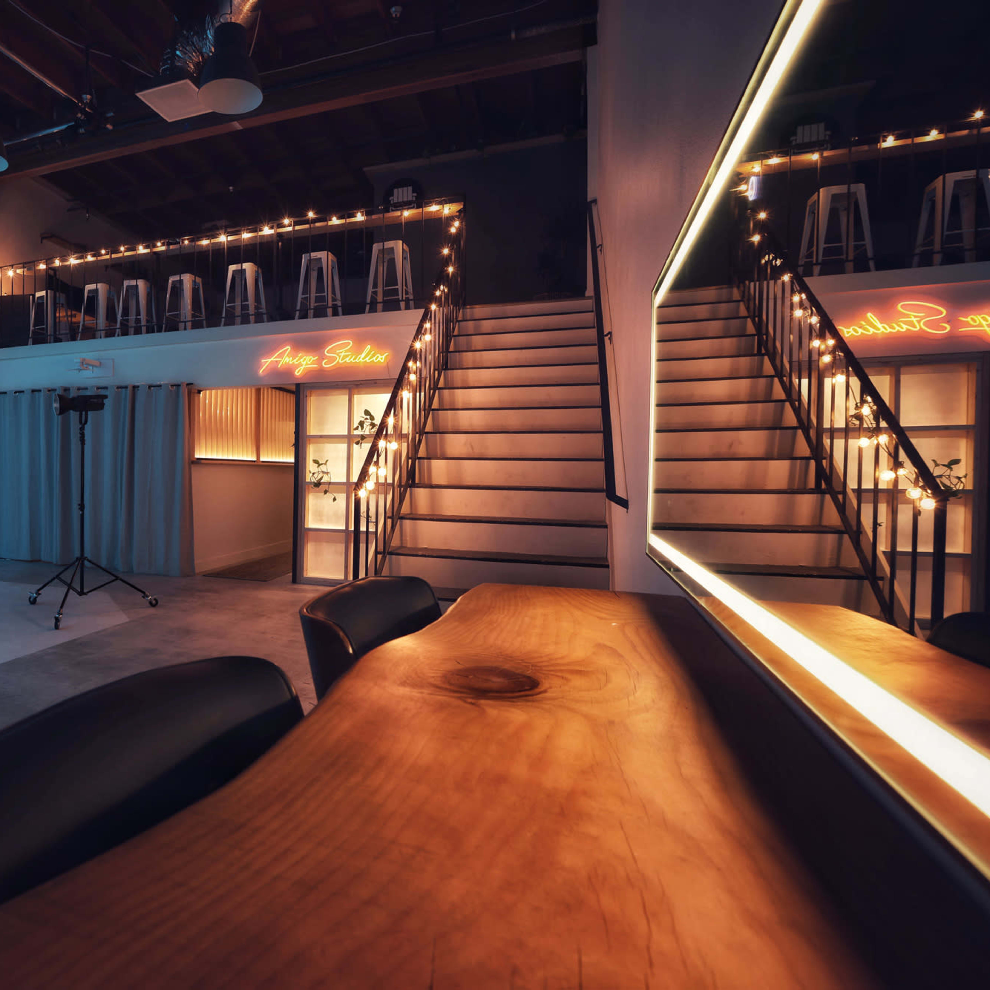 A modern studio space with a blue-lit backdrop, a staircase leading to an upper level, and a wooden table in the foreground.