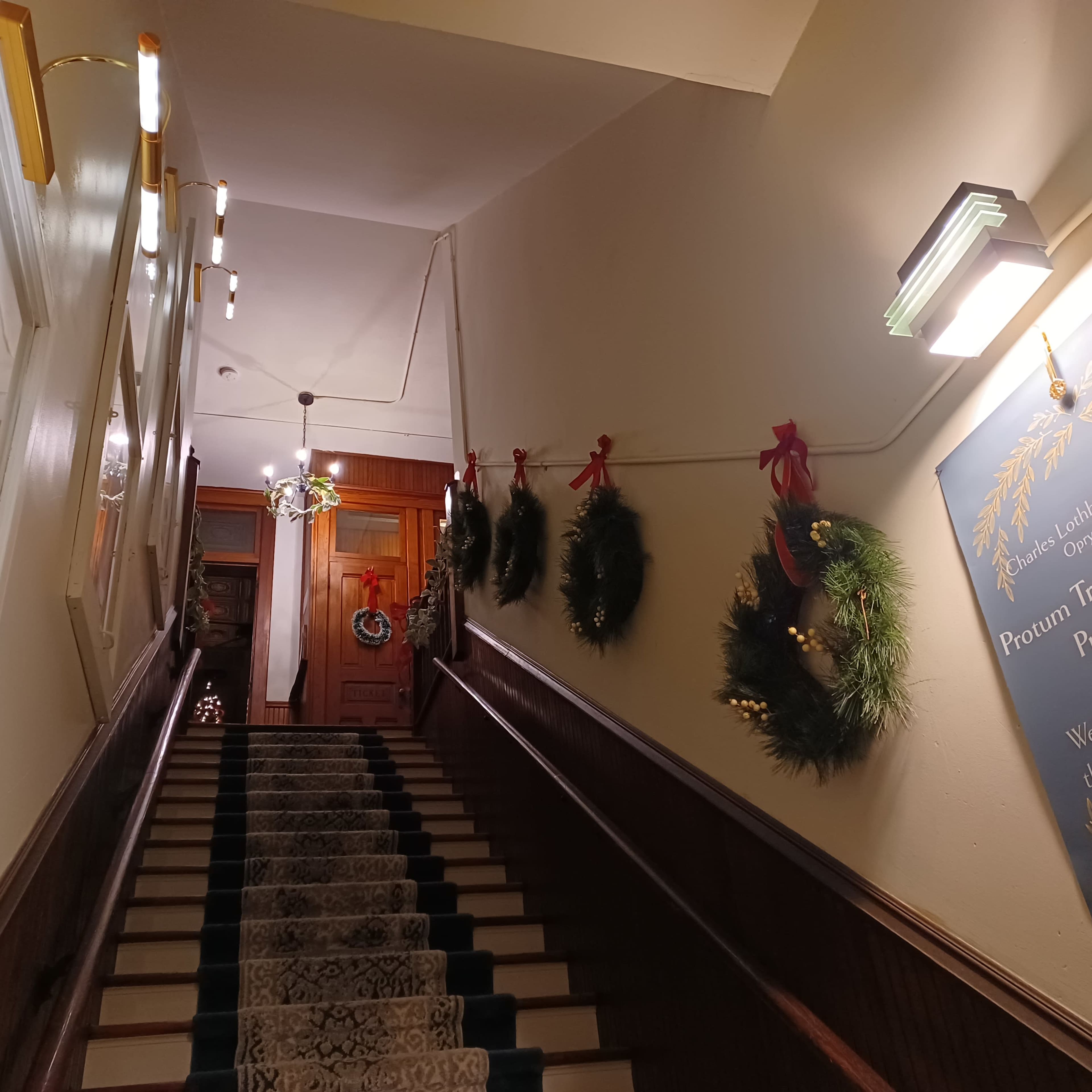 A staircase leads upward, adorned with wreaths and holiday decorations, with signs on the walls providing information and festive cheer.
